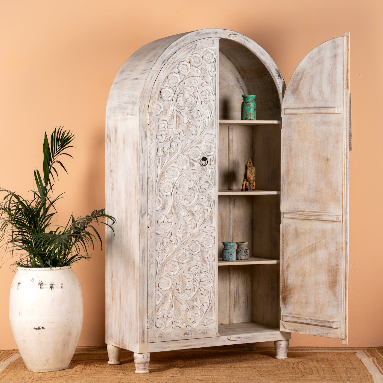 Open door image of an arched wooden wardrobe made of mango wood with hand-carved floral details; hand carved wooden furniture in Ibiza style, 190 × 100 × 40 cm.