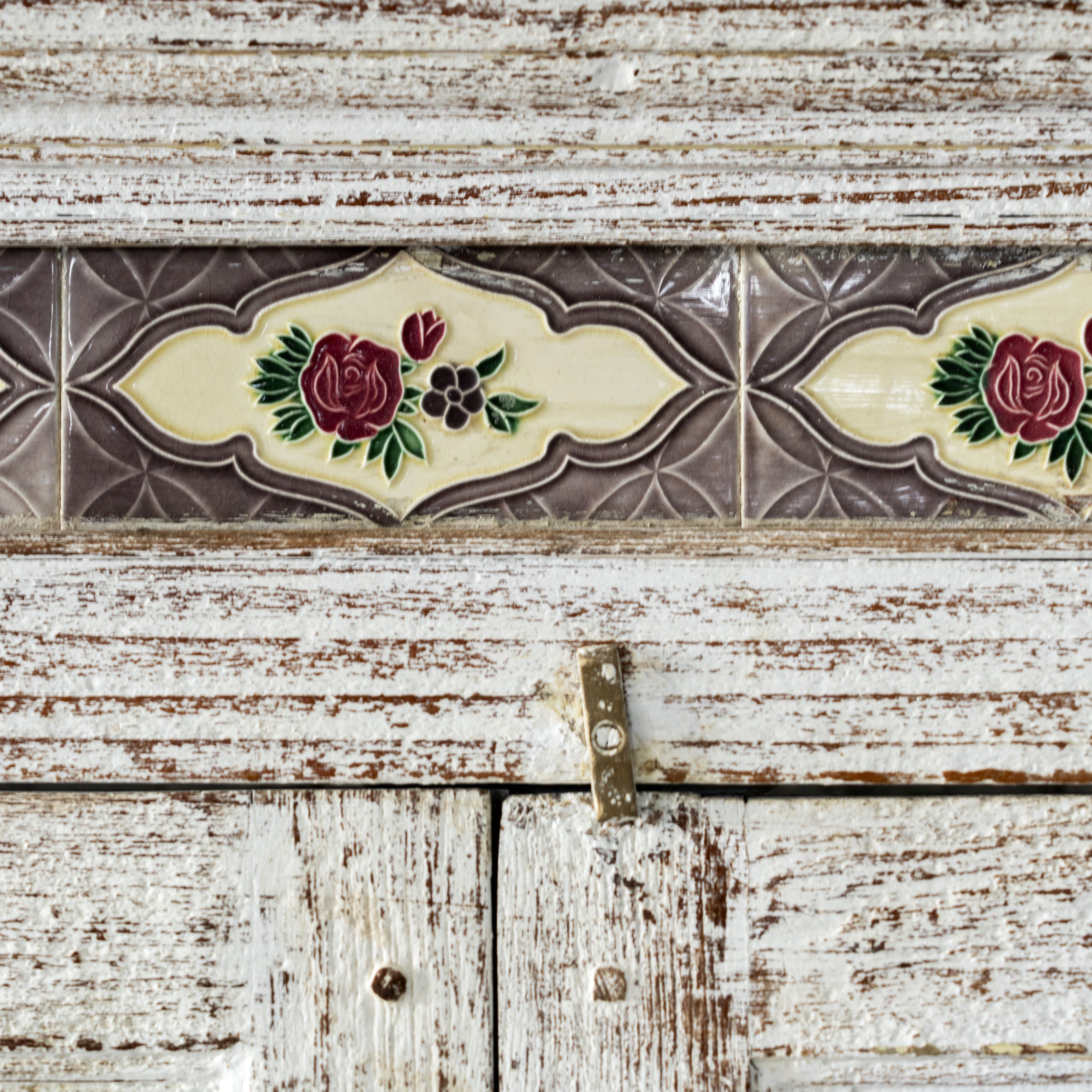 Close up image of a reclaimed teak wood cabinet in shabby chic white with glass doors and ceramic inlays – dining room furniture with vintage elegance.