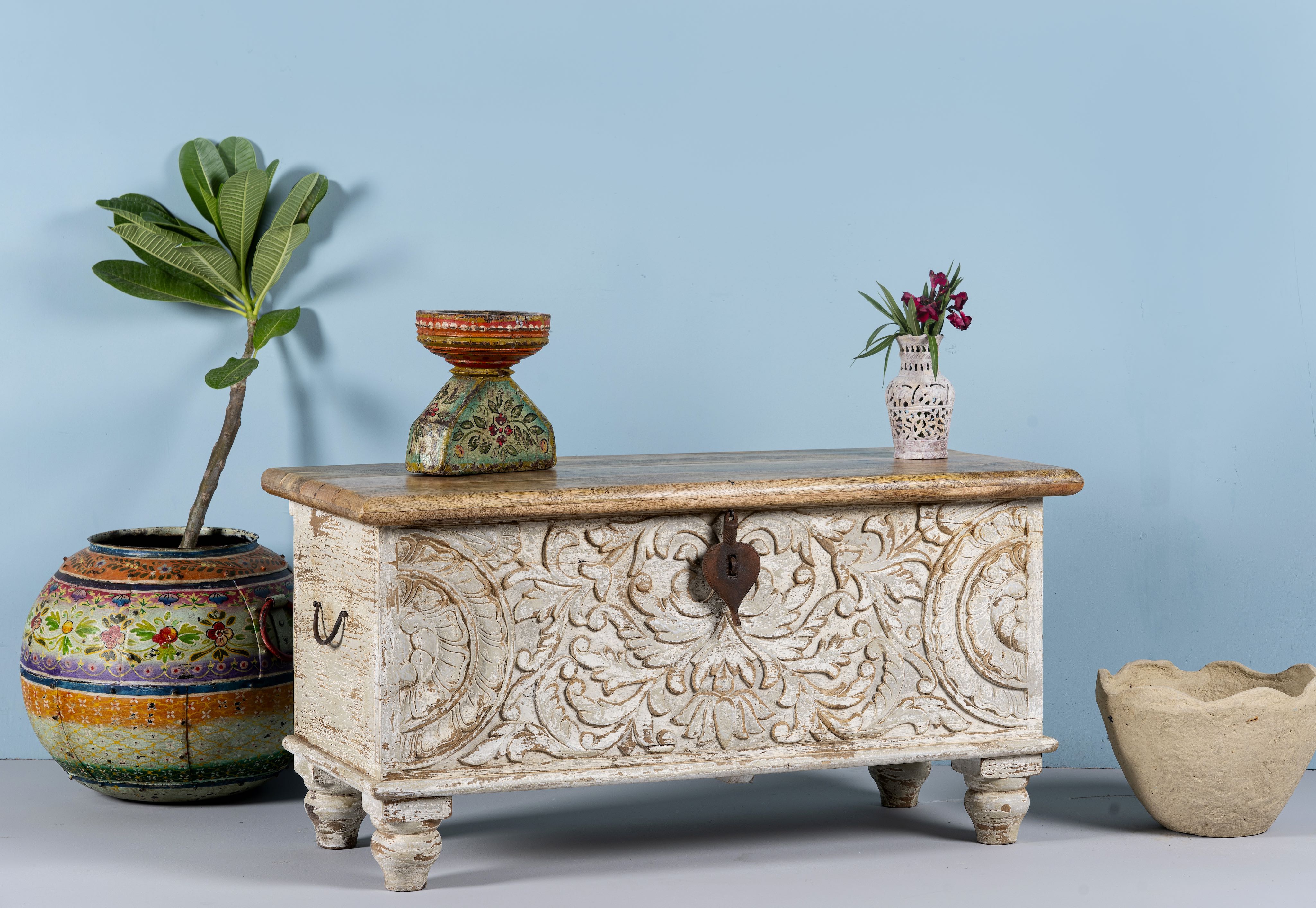 Side angle image of a hand-carved mango wood chest box with floral whitewashed detailing and iron handles – vintage home accessory and unique furniture with rustic charm.