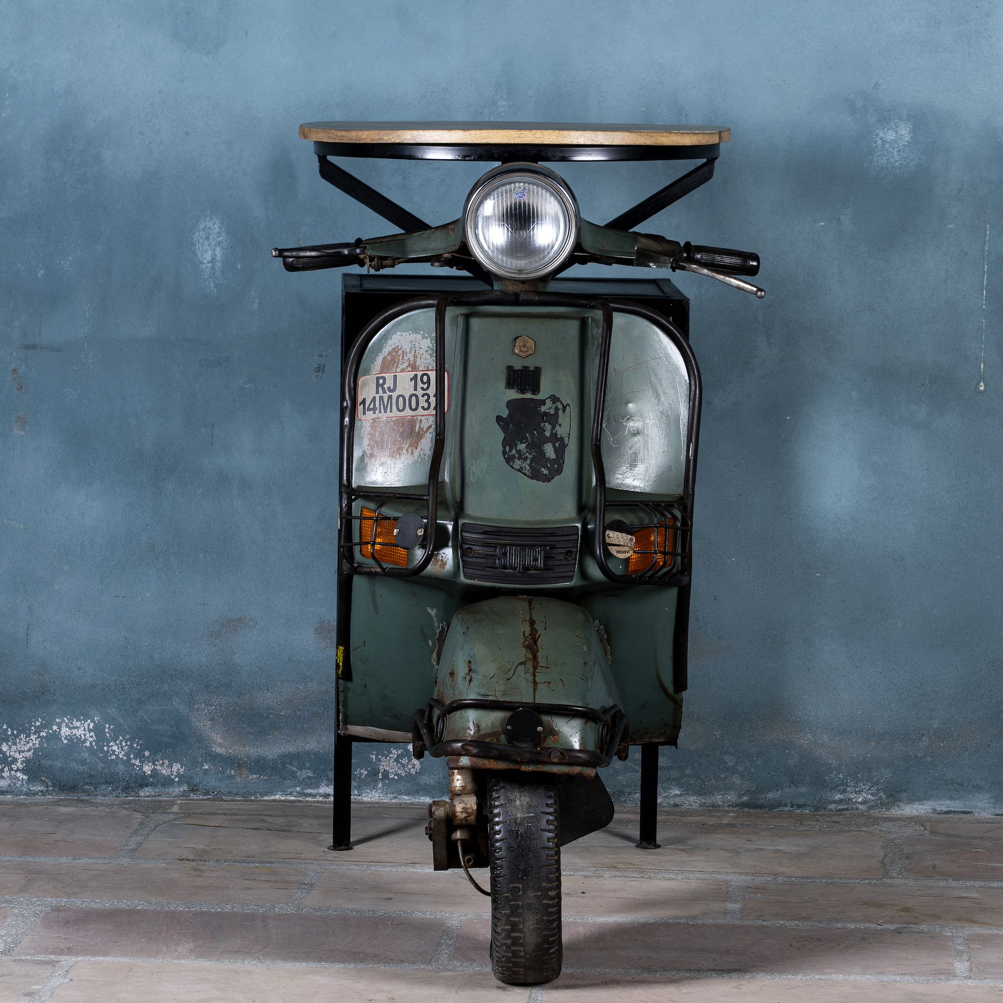 Front image of a short bar table crafted from the front half of an original Bajaj scooter, featuring a round wooden top, metal frame, and rustic industrial finish.