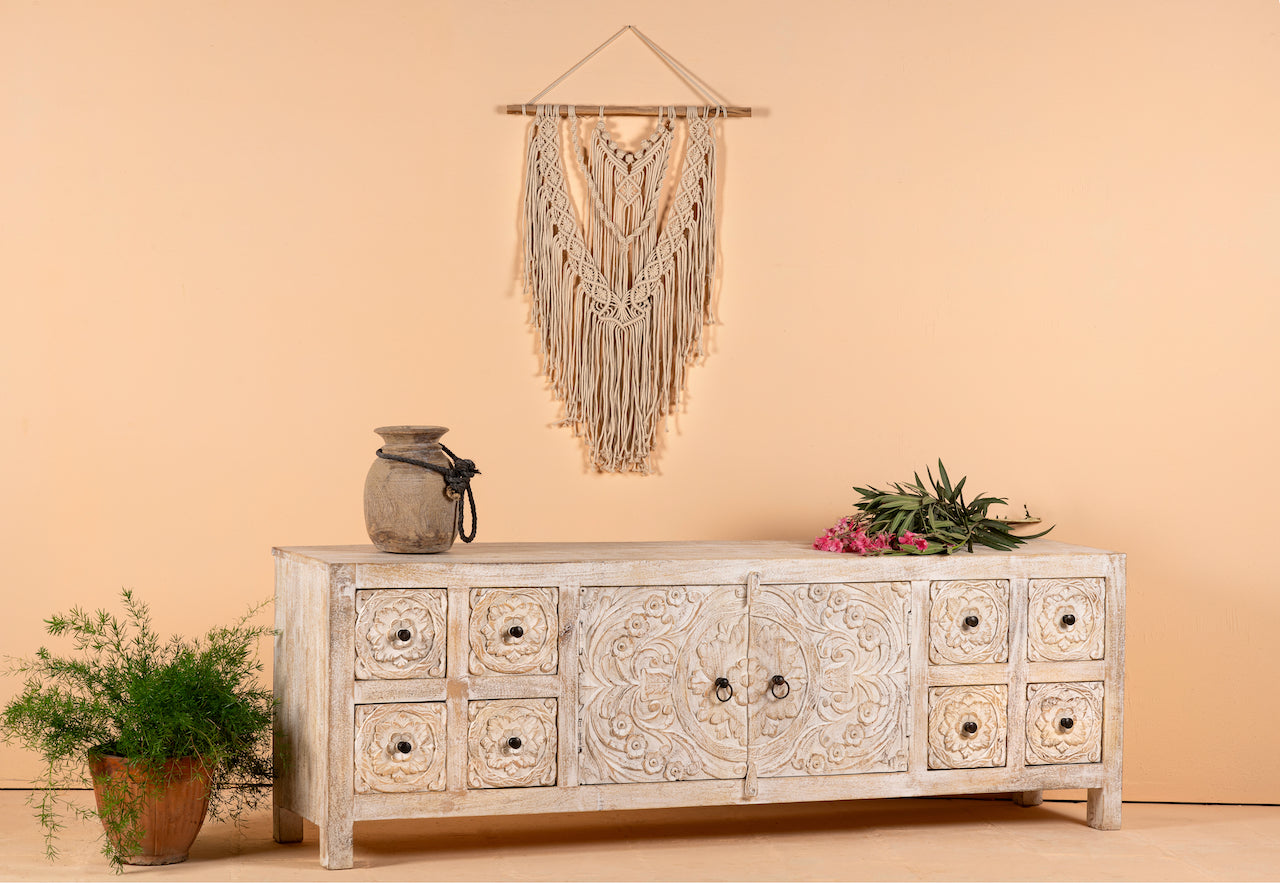 Side angle image of a whitewashed mango wood lowboard with hand-carved floral details, eight drawers and two compartments; ideal as a wooden lowboard or carved wood console table, 180 × 60 × 40 cm.