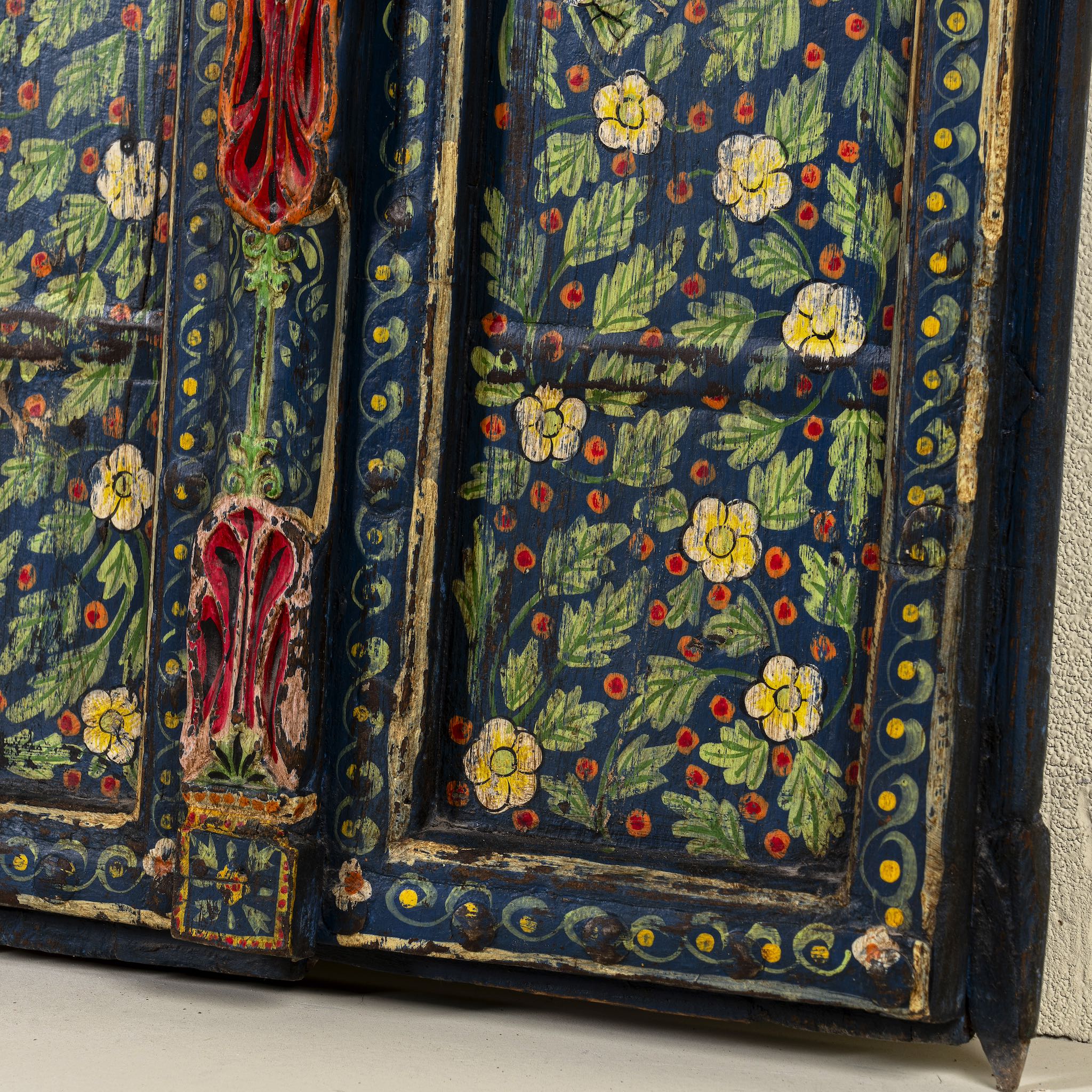 Side angle image of a decorative wall panel made from an old teak wood window frame, hand-painted with intricate floral patterns in vibrant colours including green, red, yellow, and blue, showcasing traditional Indian craftsmanship and vintage charm.