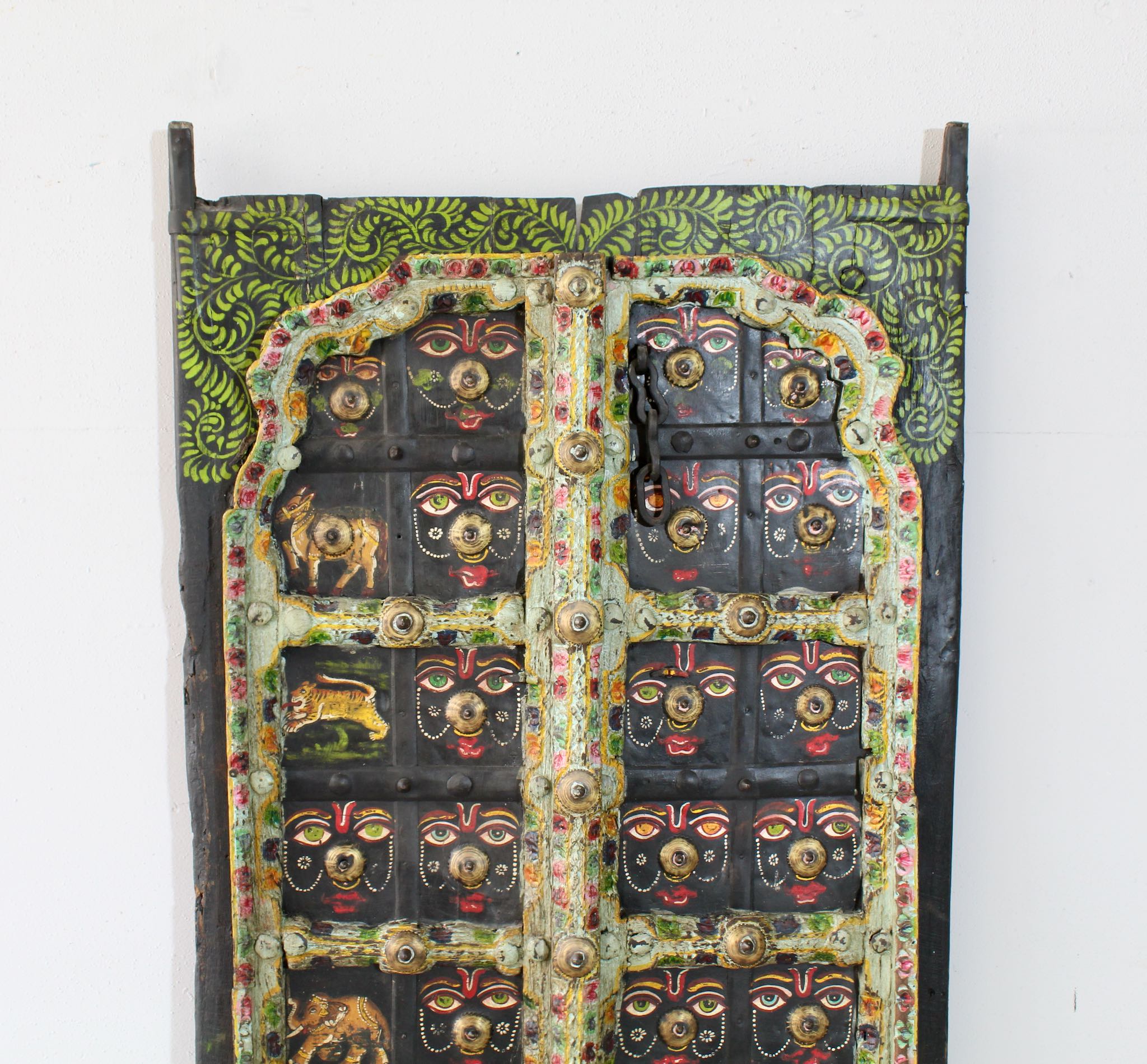 Close up image of a Ayandh hand-painted teak door panel featuring sacred animal motifs and folk figures with a weathered floral frame—a vibrant example of teak door panels and unique Indian wall decoration.