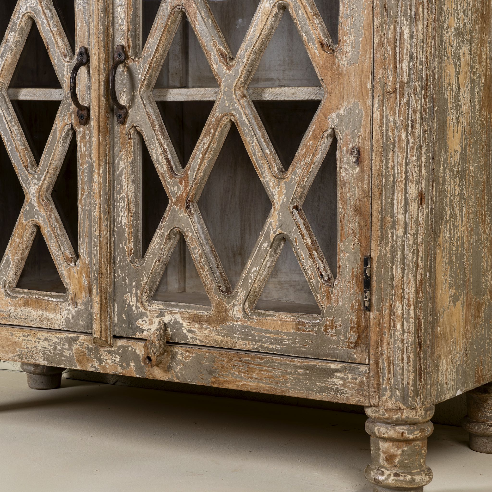 Close up image of the leg part of a vintage display cabinet made from solid mango wood with glass doors and shelving – handcrafted Ibiza-style showcase with carved details.