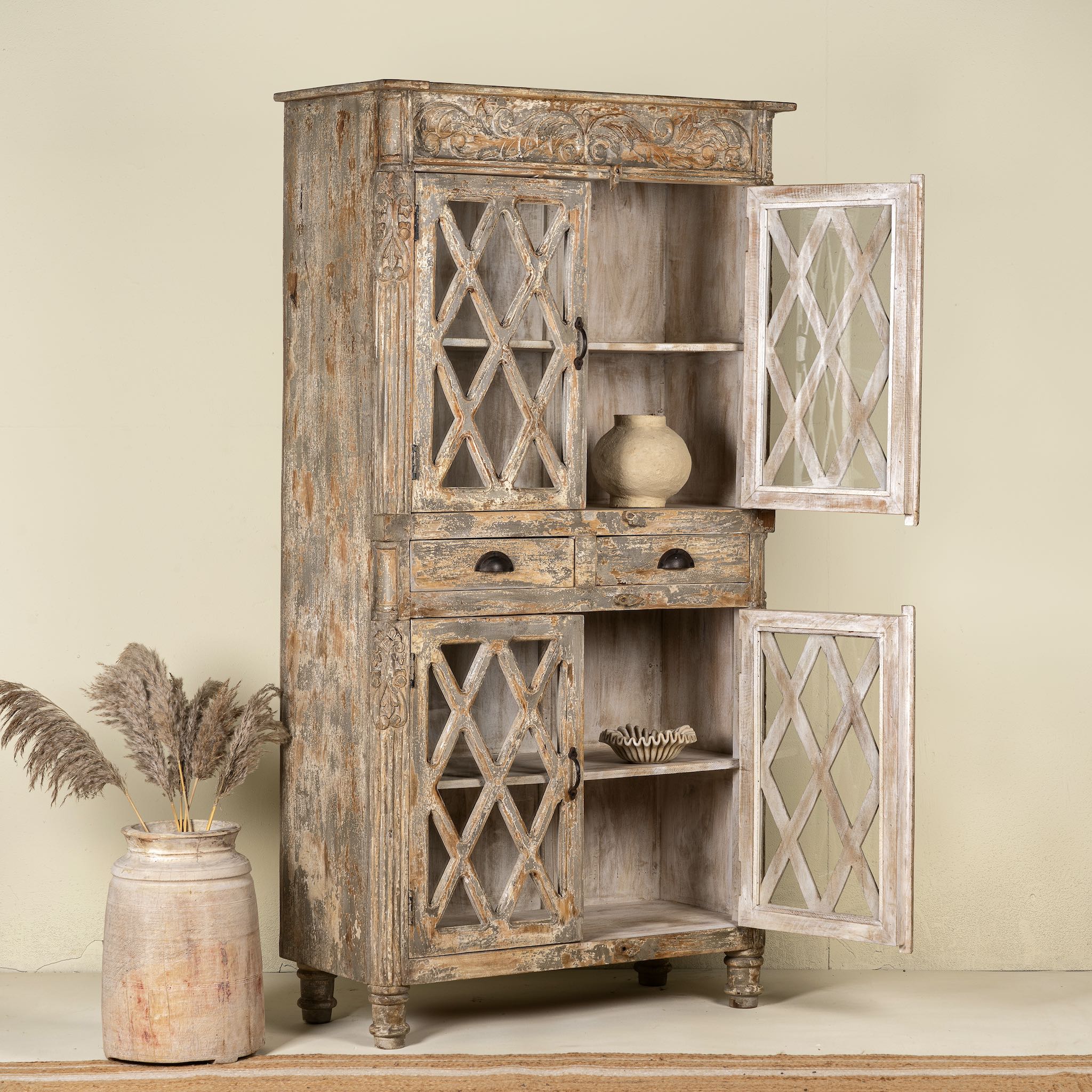 Side angle image with open doors of a vintage display cabinet made from solid mango wood with glass doors and shelving – handcrafted Ibiza-style showcase with carved details.