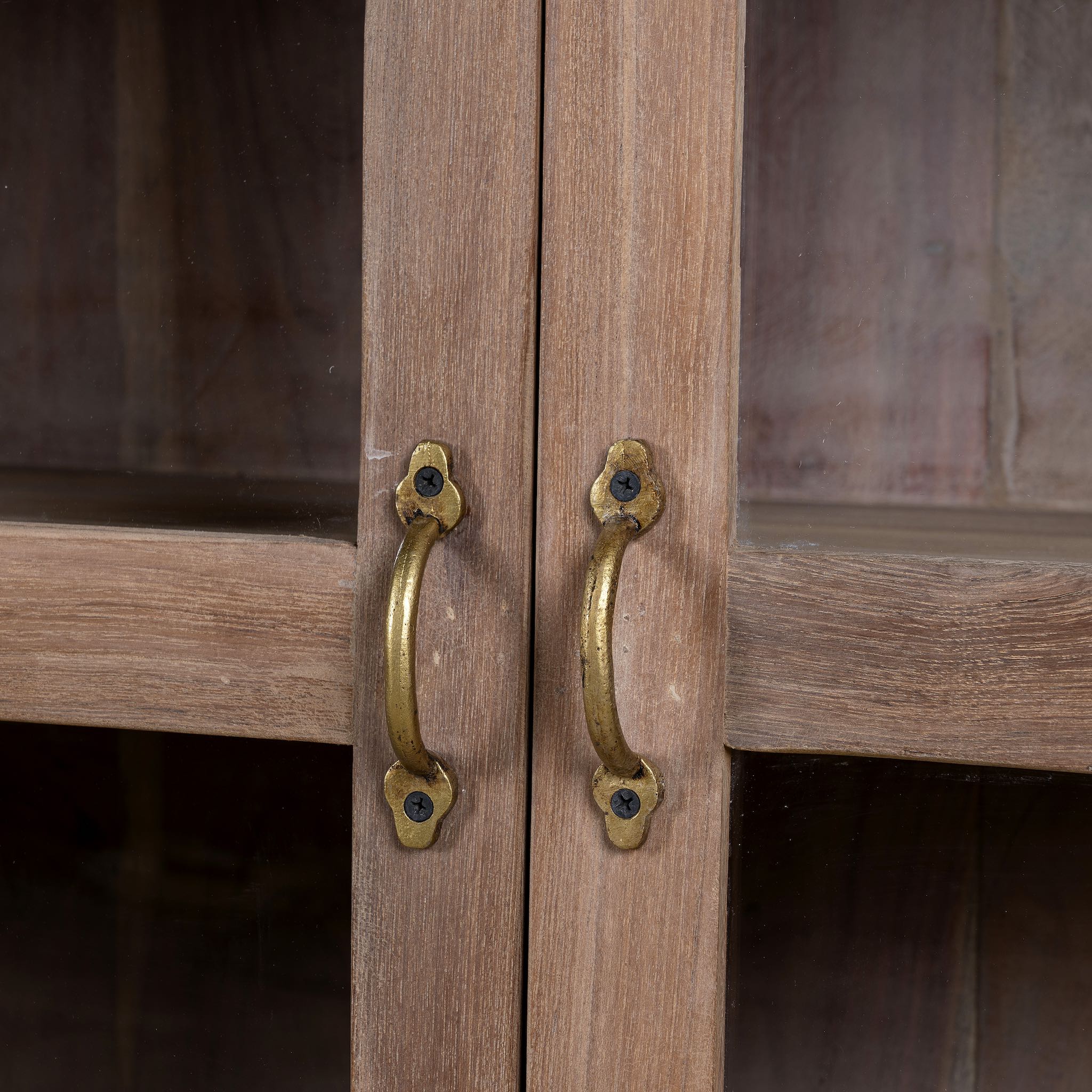 Close up image of the handles of a rustic showcase cabinet made from recycled teak wood, featuring four glass-paneled doors with brass handles and a lightly weathered finish, offering a warm, natural look ideal for displaying decor or tableware.