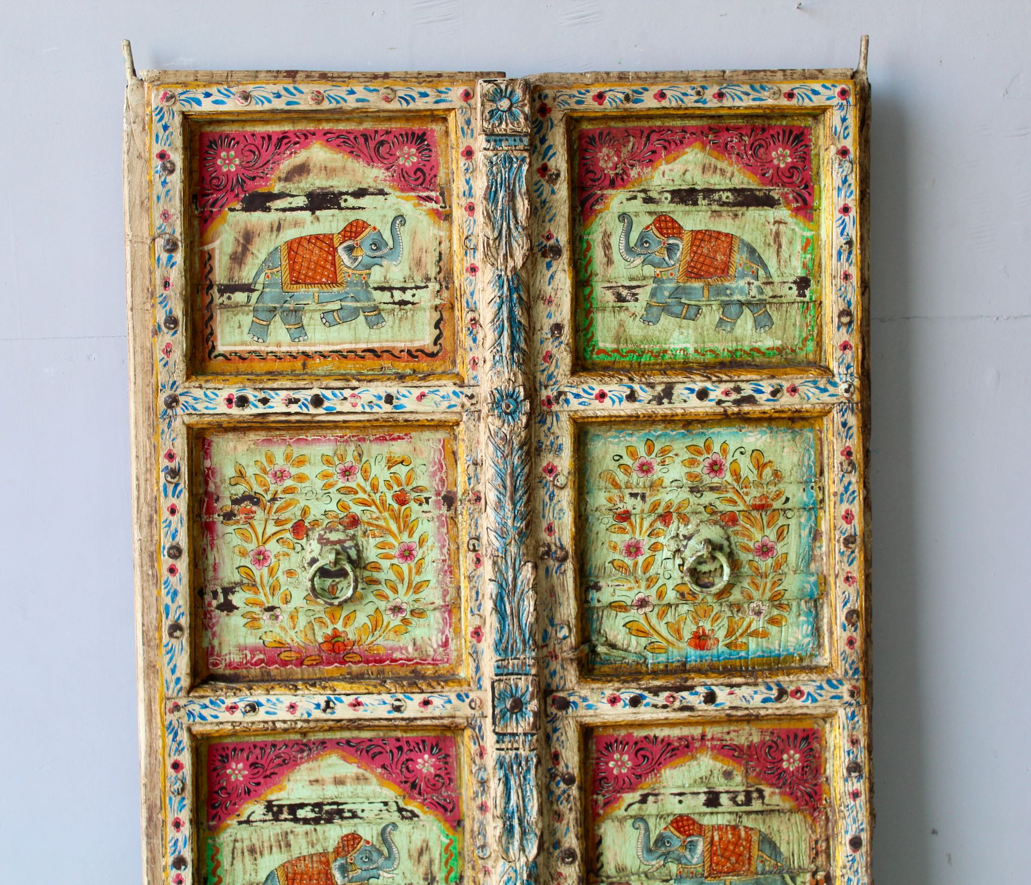 Close up image of a hand-painted Indian antique teak door with elephant and floral motifs, distressed green finish, vintage wall panels for unique home decor.