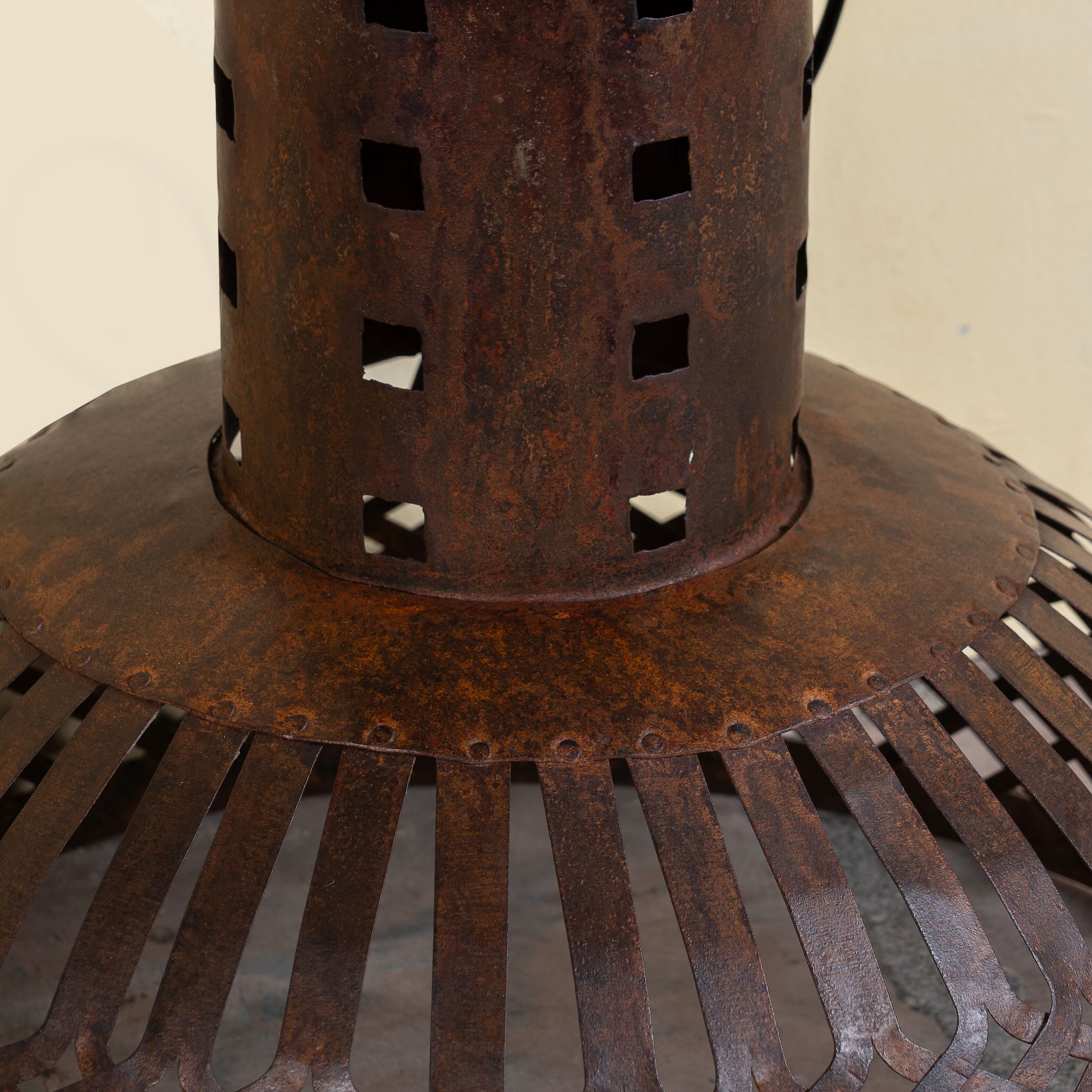Close up image of a Daya hand crafted metal pendant light with a rusted finish, featuring a ventilated cylindrical top and wide dome with lattice detailing—an artisan addition to metal pendant lights and industrial hand forged lamps.