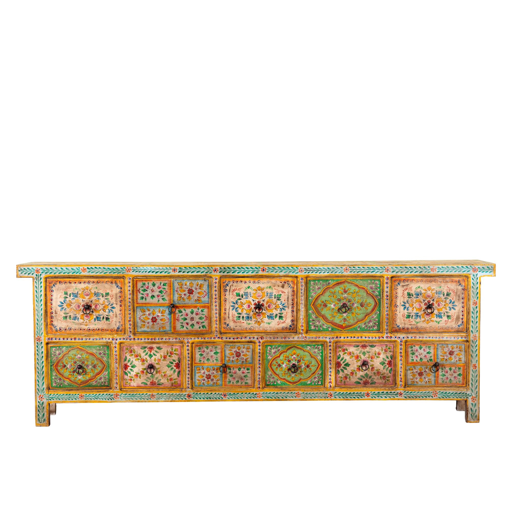 White background image of a hand painted mango wood chest of 11 drawers with floral motifs; artisanal mango wood furniture and hand painted furniture, 250 × 41 × 85 cm.