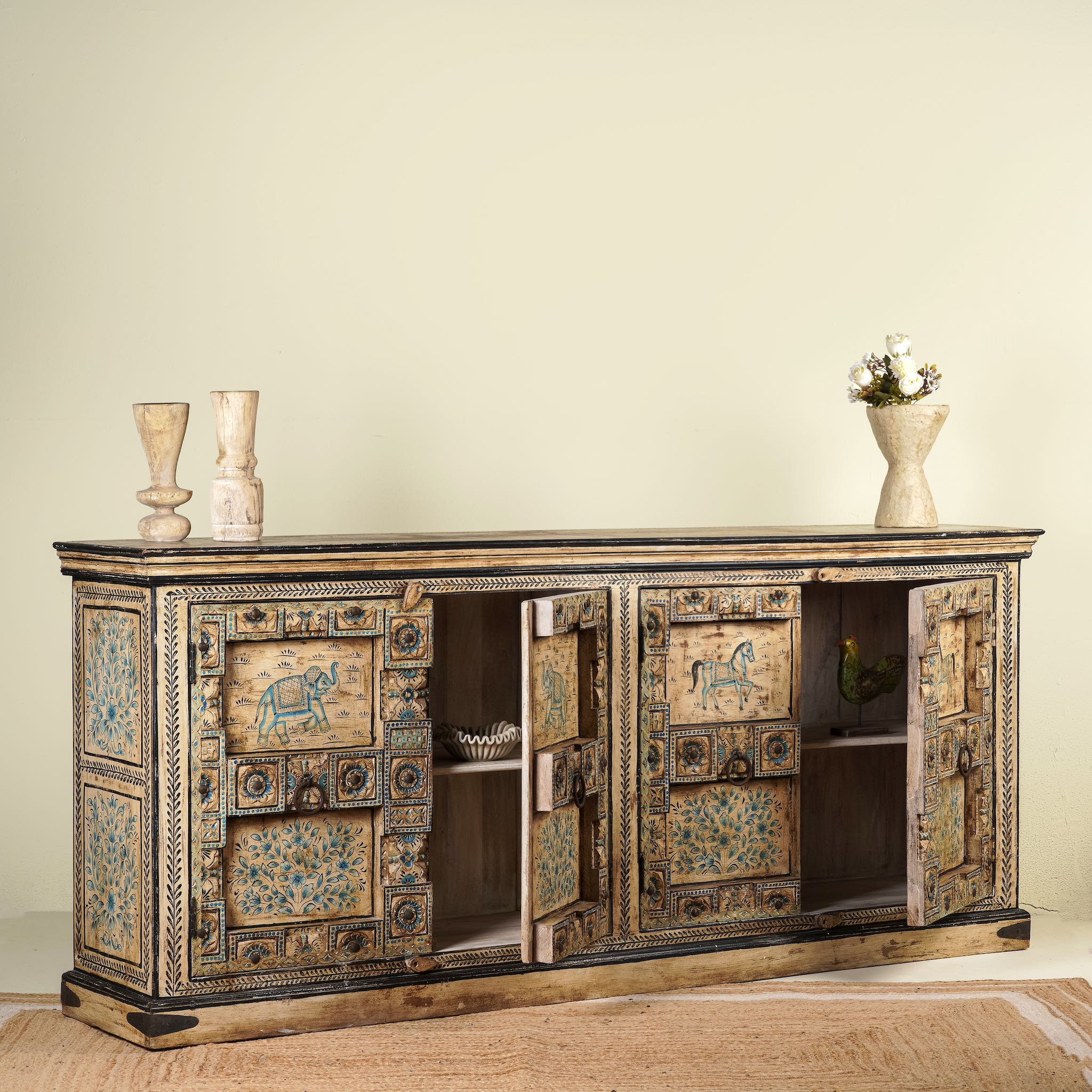 Open door image of a vintage sideboard made from teak wood, hand-painted with traditional Indian motifs including elephants, camels, horses, and floral patterns in muted teal and earthy tones, featuring detailed borders and a distressed finish.