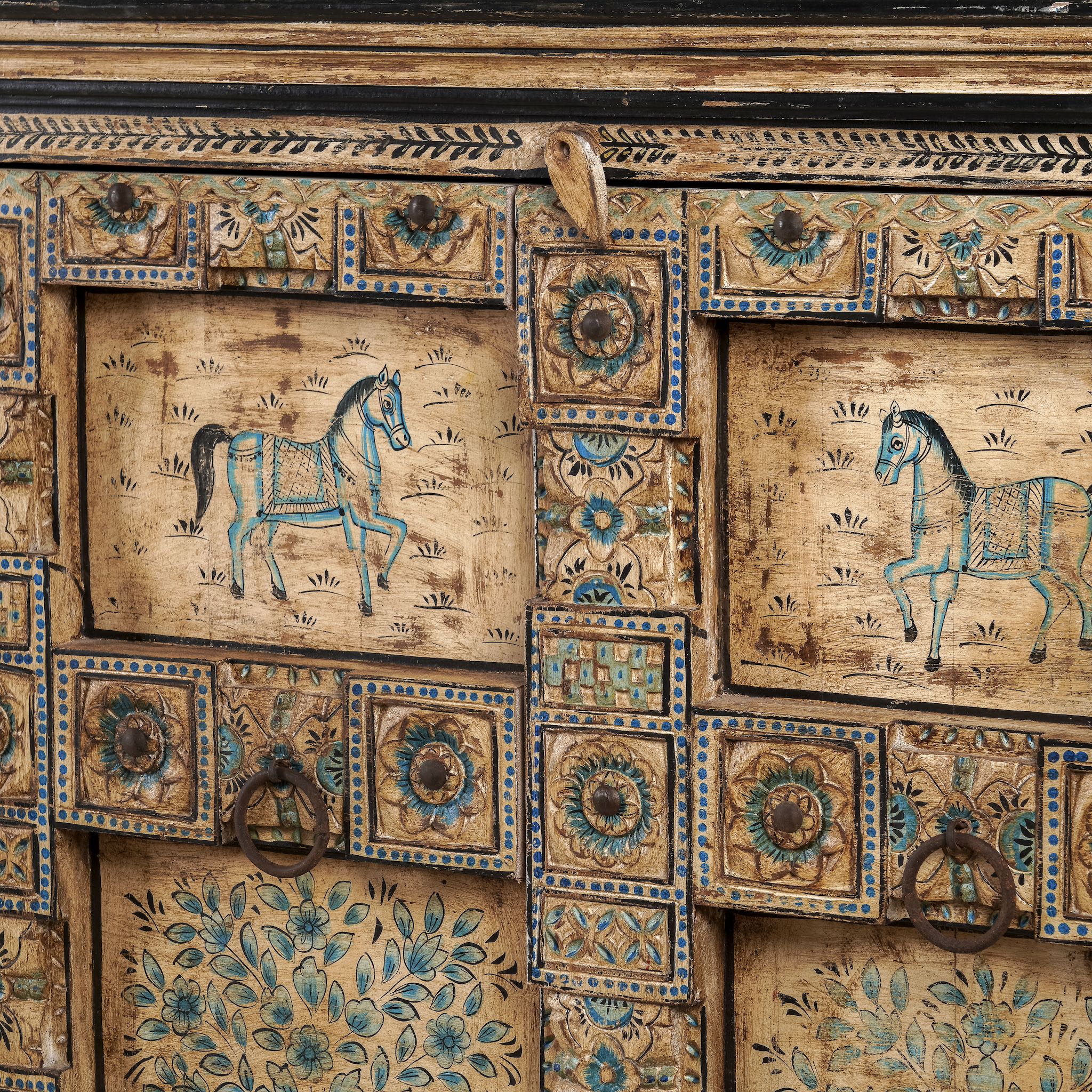 Close up image of a vintage style sideboard made from teak wood, hand-painted with traditional Indian motifs including elephants, camels, horses, and floral patterns in muted teal and earthy tones, featuring detailed borders and a distressed finish.