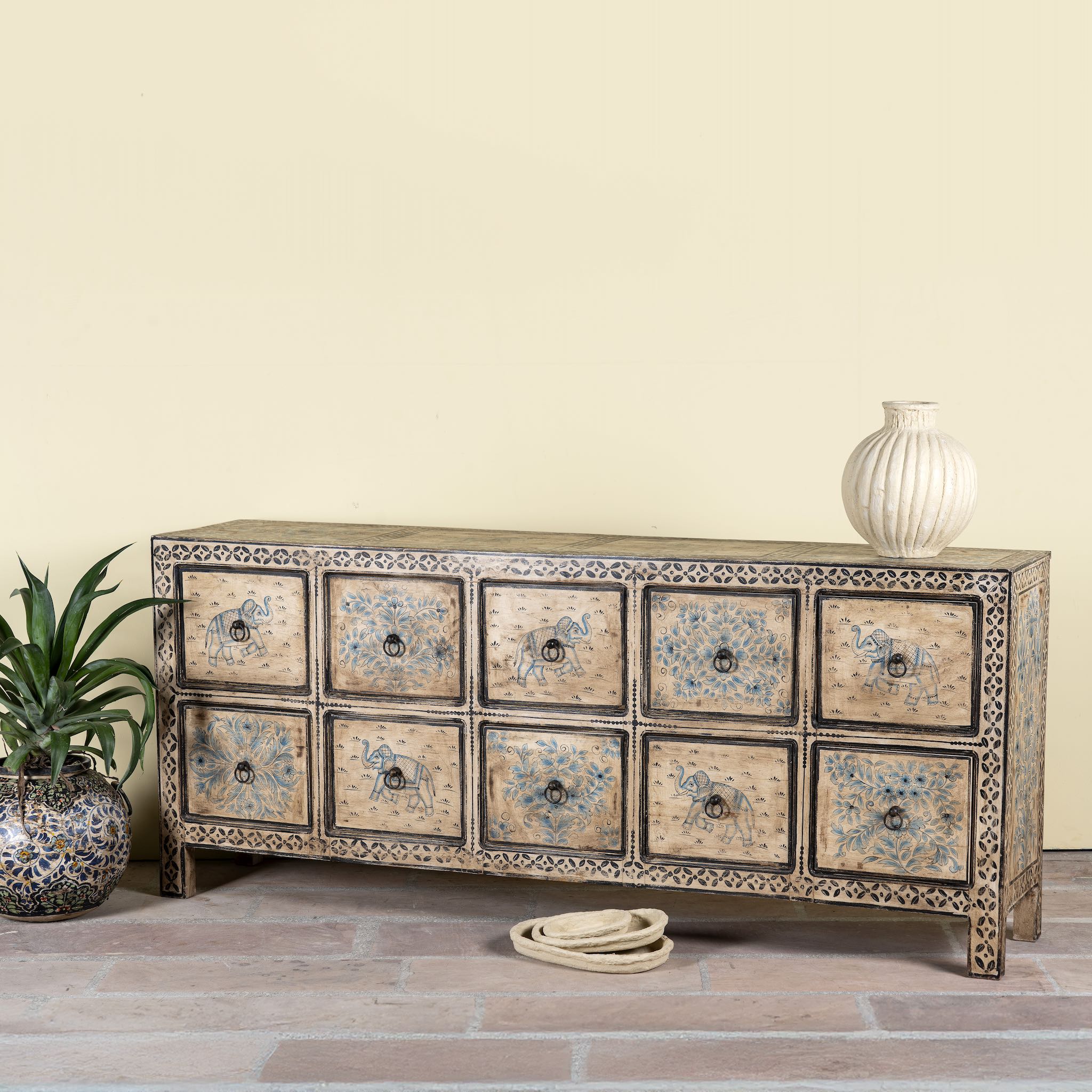 Side angle image of a hand painted mango wood chest of 10 drawers with elephant and floral motifs; hand painted furniture for a boho chic living room, 200 × 41 × 85 cm.