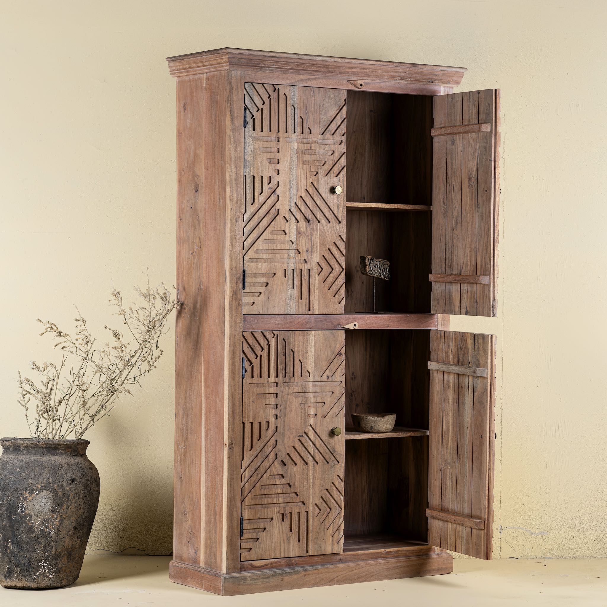 Open door view of a hand crafted acacia wood cabinet with 4 doors, brass fitted door knobs and geometrical carvings.
