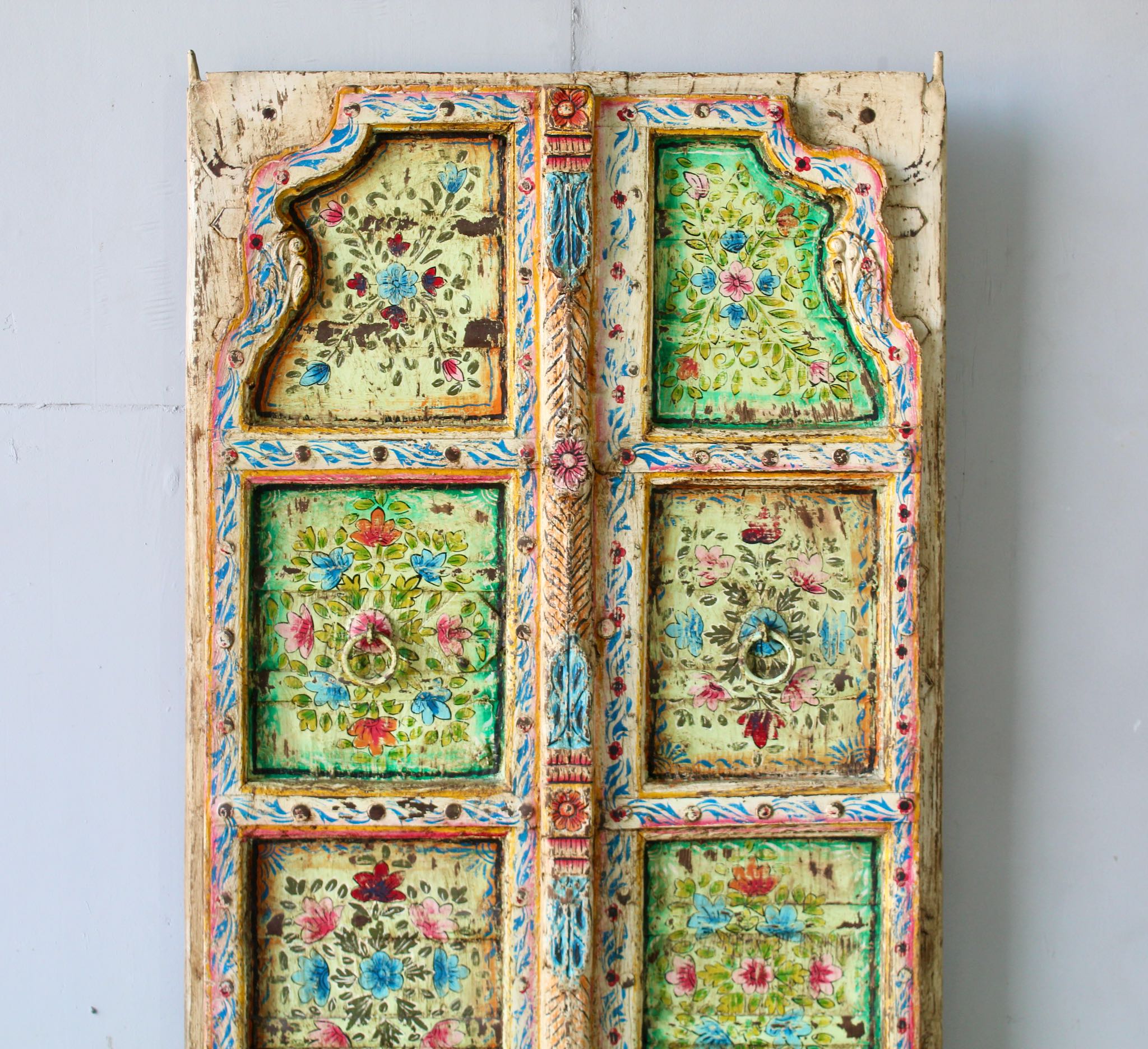 Close up image of a Gitra hand-painted teak door panel featuring floral motifs in soft pastels and a carved arched frame—an elegant and unique Indian wall decoration repurposed from antique architecture.