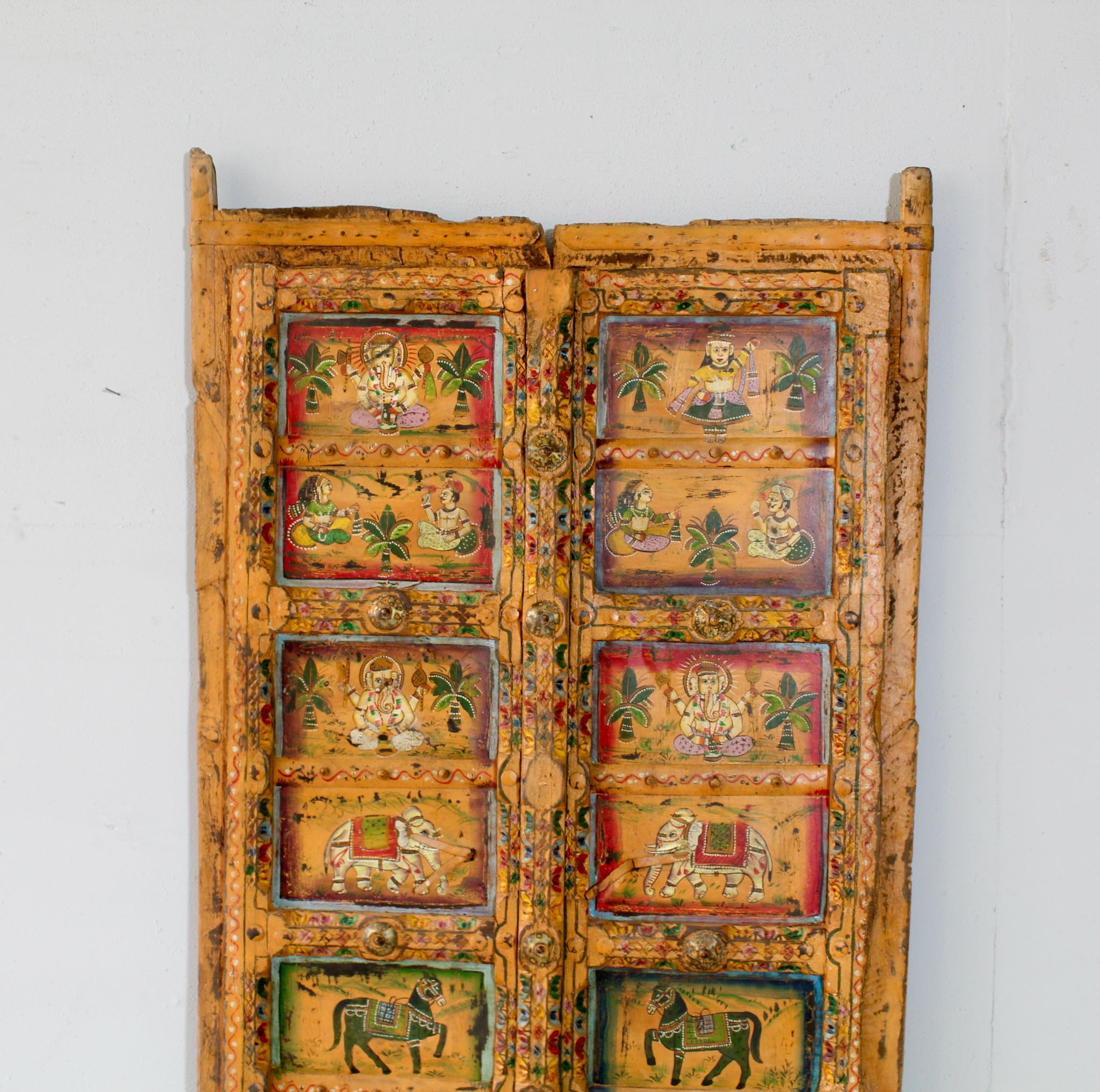 Close up image of a Indian painted door decoration featuring mythological and village scenes on reclaimed teak—an artisanal Indian door panel with folk motifs and vintage patina.