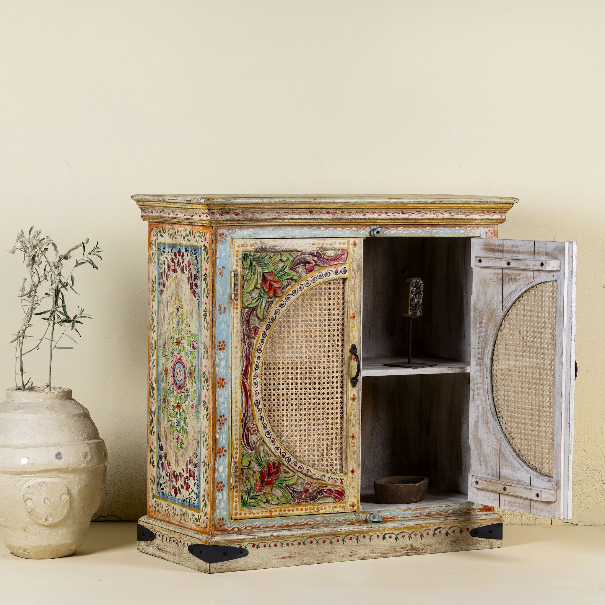 View with open doors of a hand-painted, hand-carved cupboard made of mango wood with floral design and rattan inserts.