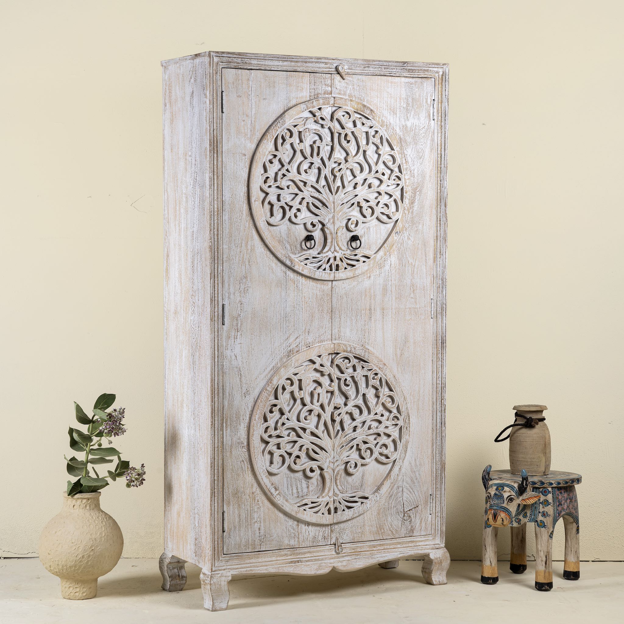 Side angle image of a white washed armoire with hand-carved Tree of Life motif, mango wood carved wood furniture with storage, 90 × 40 × 180 cm.