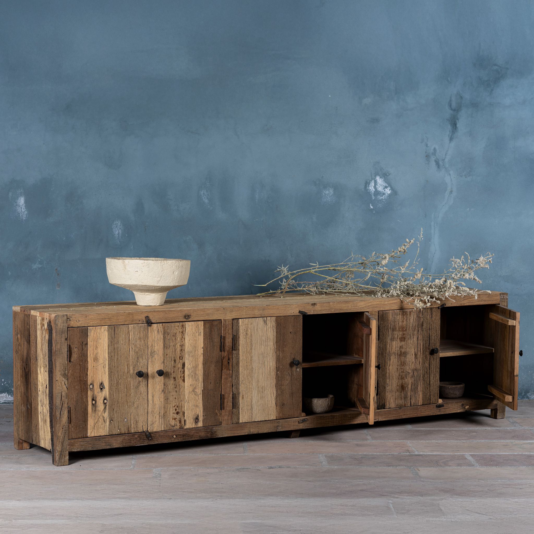 Side angle image of a sustainable driftwood furniture lowboard made from reclaimed wood with four cabinets and rustic finish; 230 × 45 × 60 cm.