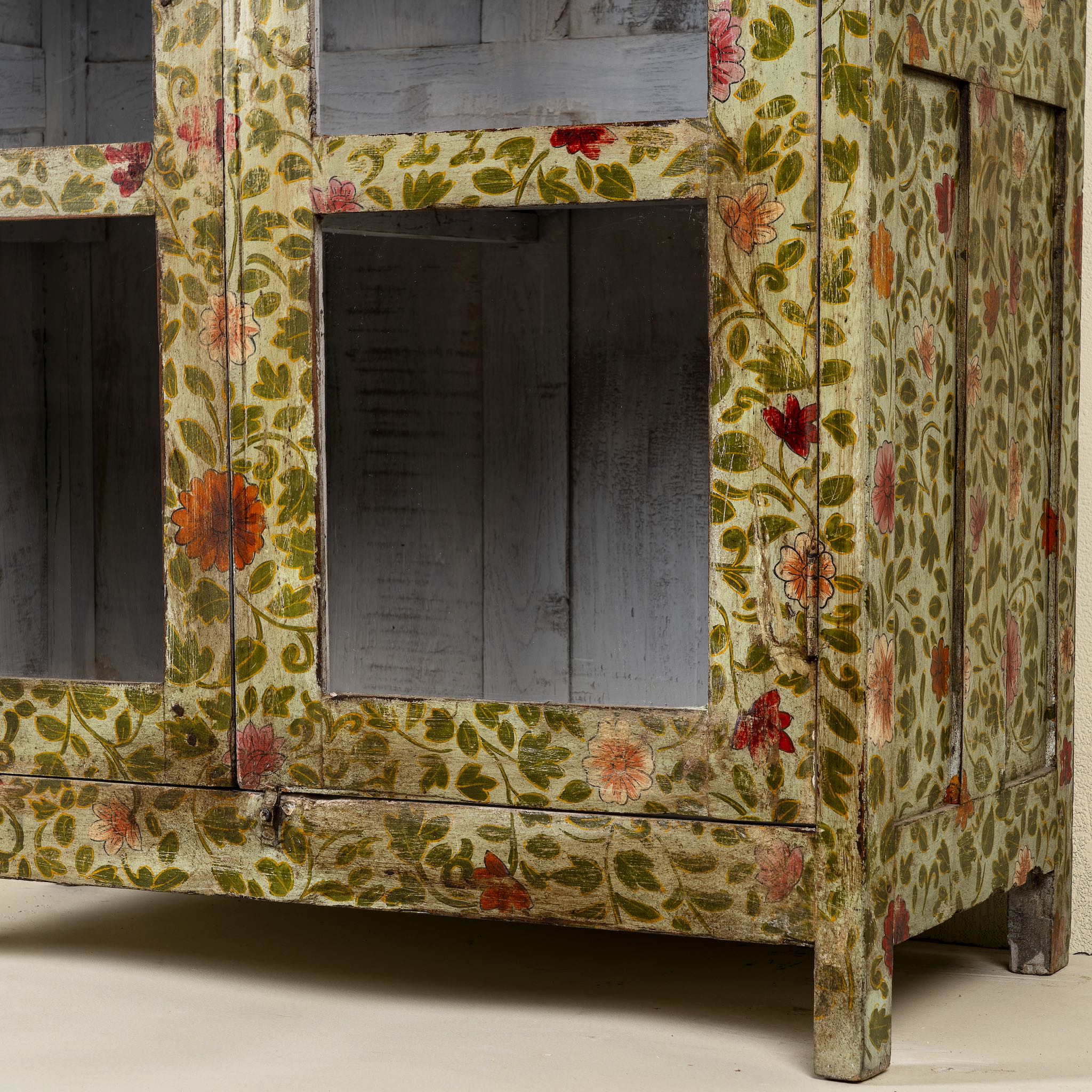 Close up image of a hand-painted reclaimed wood cabinet with glass doors and floral motifs – sustainable and artistic furniture for vintage or bohemian interiors.