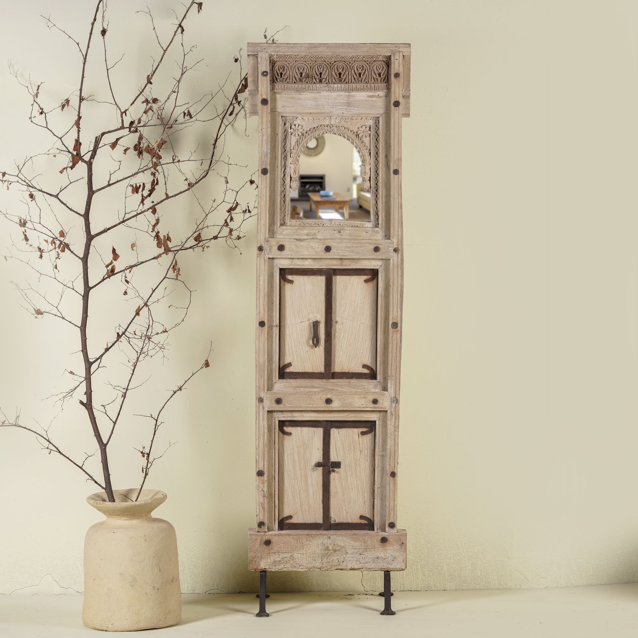 Mirror stand crafted from reclaimed teak wood with intricate carved detailing and two storage cabinets, set on a sturdy iron base, blending rustic charm with vintage Indian architectural elements.