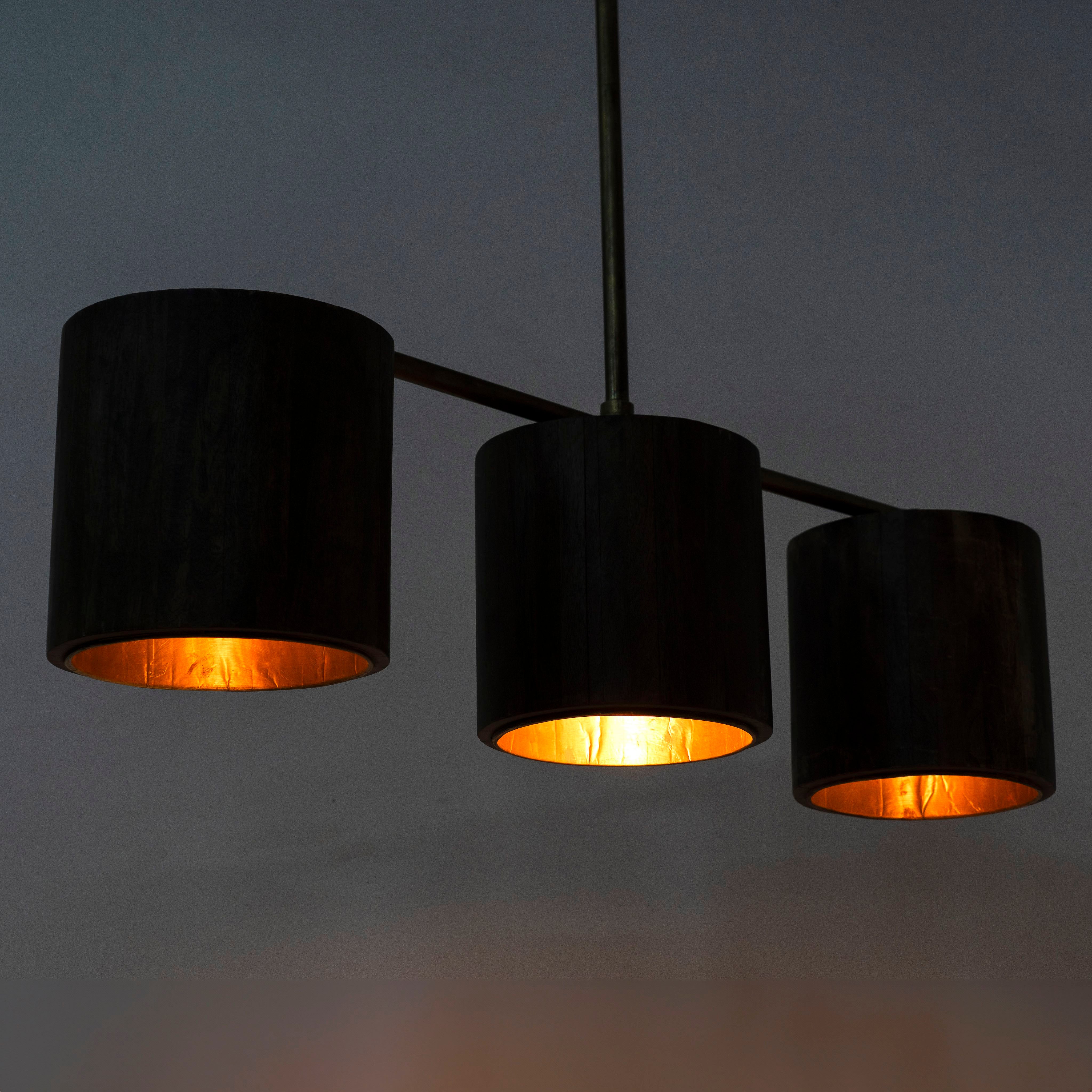 Image showing a lighted version of a long wooden pendant light with brass-lined interior and three lights – vintage lighting with natural grain finish, perfect for kitchens, dining areas, or living rooms.