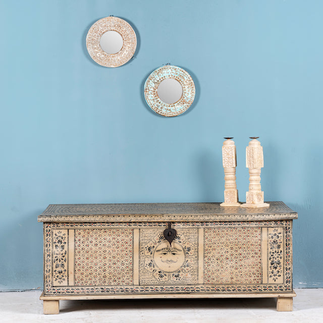 A hand-painted reclaimed wood storage chest with intricate Indian motifs, displayed against a blue wall with two decorative mirrors above it.
