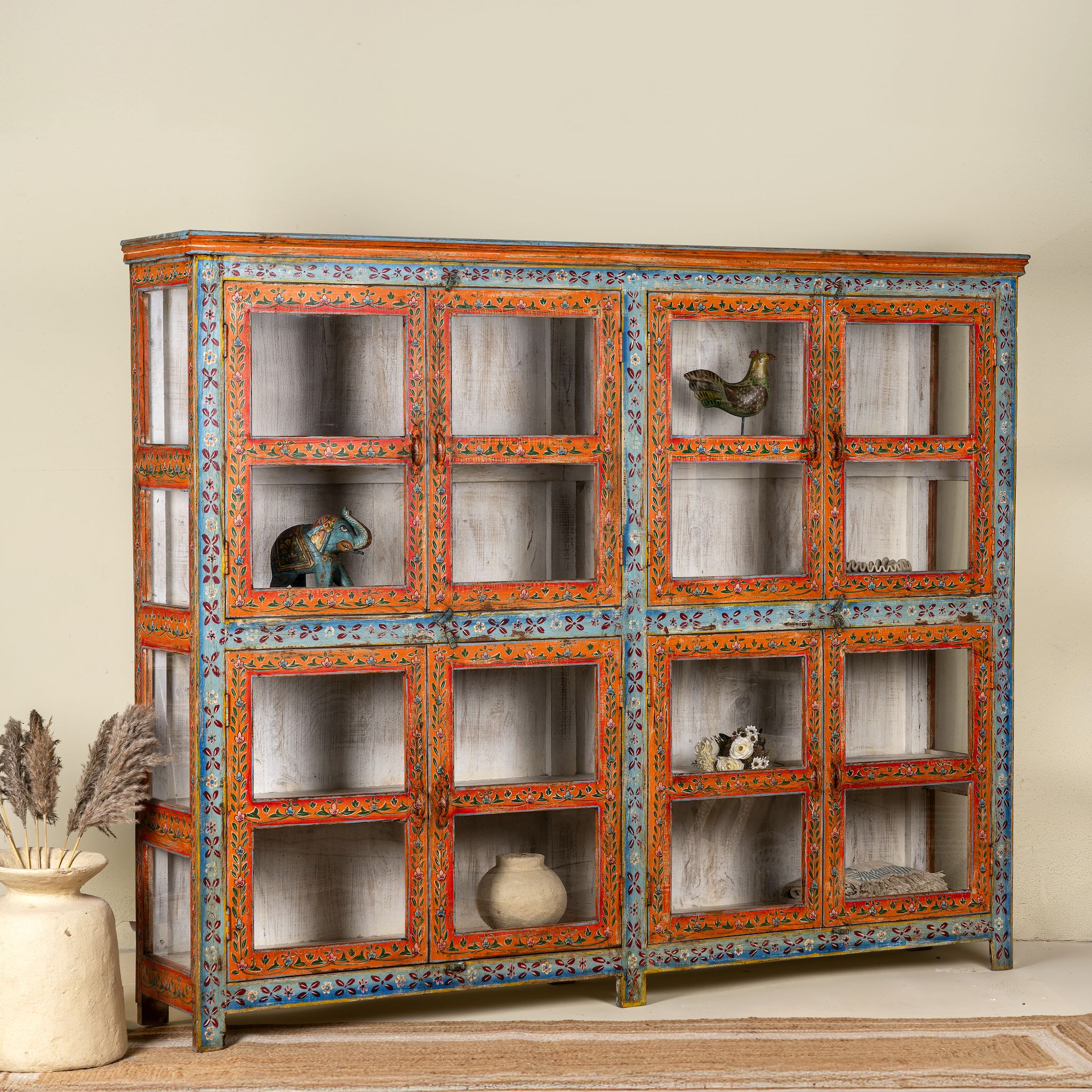 Side angle image of a hand-painted reclaimed wood showcase cabinet with Ibiza-style motifs, glass-panelled doors, unique wooden furniture for living room, 213 × 40 × 170 cm.