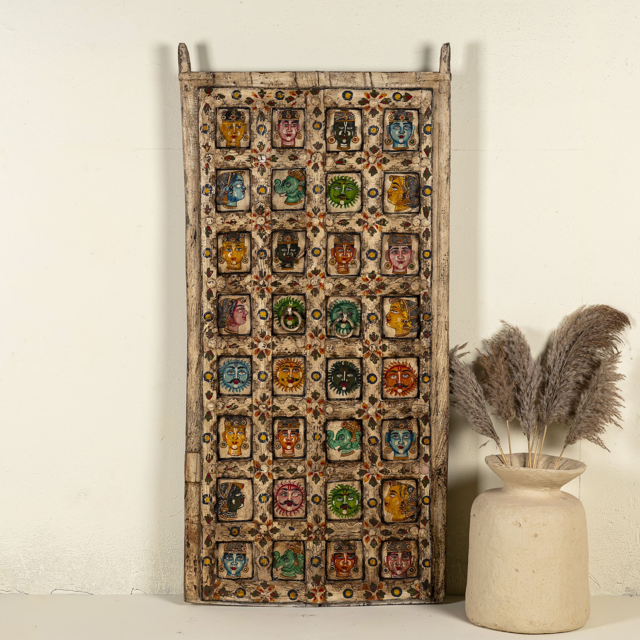 Tall vintage wall panel made from reclaimed teak wood, intricately hand-painted with a grid of vibrant deity faces, animals, and symbolic motifs in rich colours, each framed within carved squares, reflecting traditional Indian folk art.