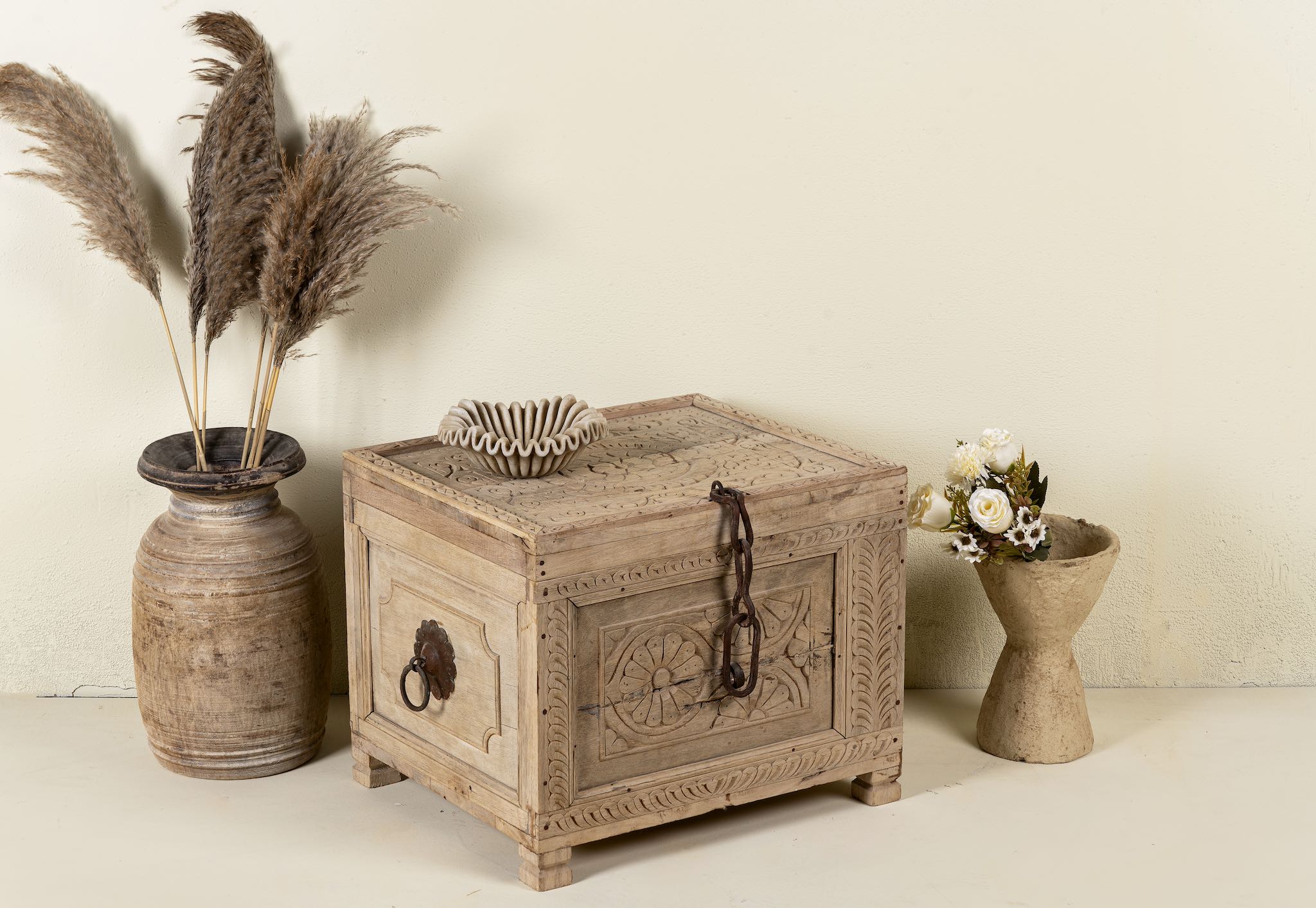 Side angle image of a hand-carved storage chest made from reclaimed teak wood, showcasing intricate floral and geometric patterns on all sides, with a rustic natural finish and a vintage-style iron latch and handles.
