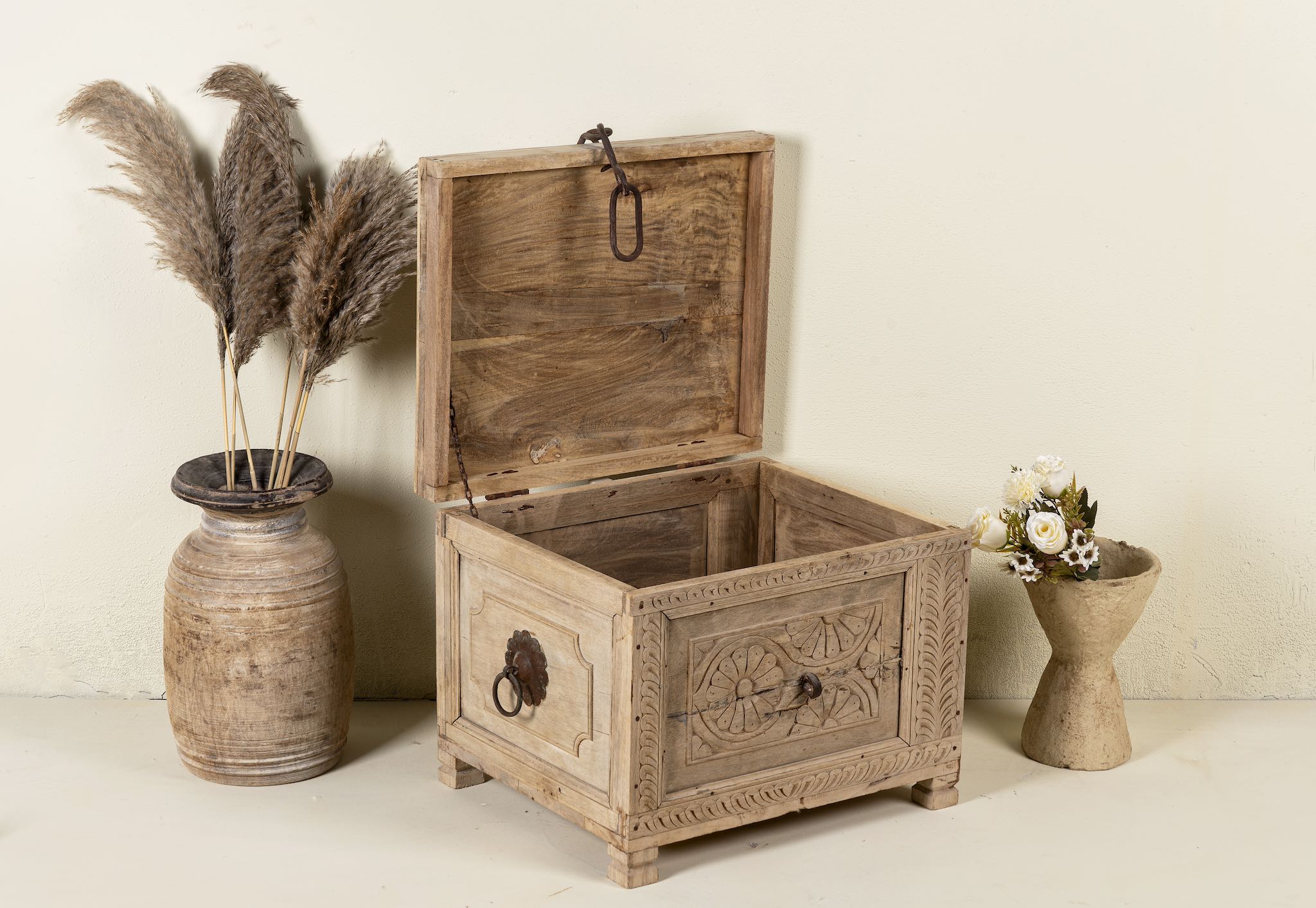 Side angle image with open lid of a hand-carved storage chest made from reclaimed teak wood, showcasing intricate floral and geometric patterns on all sides, with a rustic natural finish and a vintage-style iron latch and handles.
