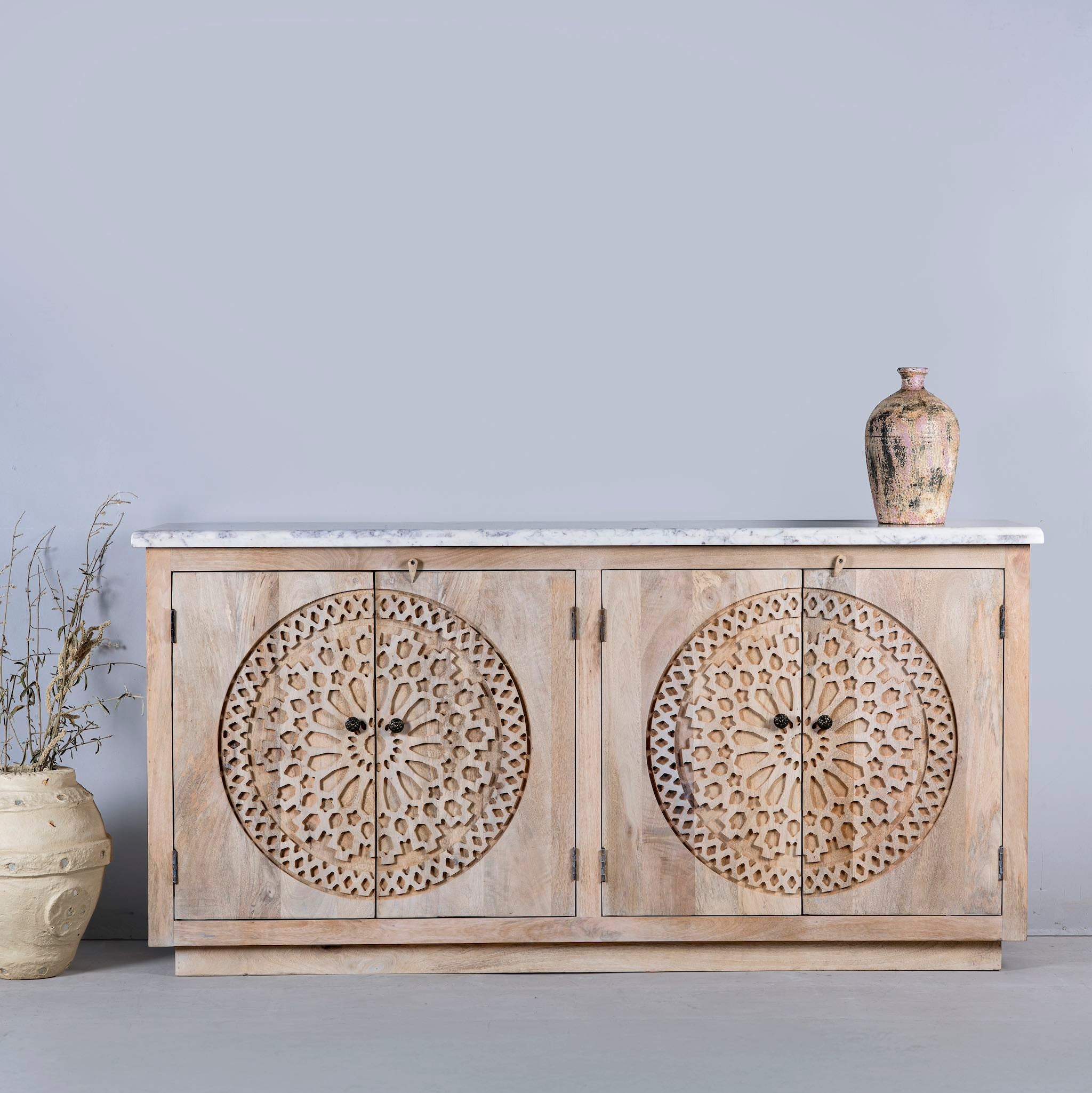 Front view of a Acacia wood sideboard with circular carvings, 4 doors and iron handles with a white marble top.