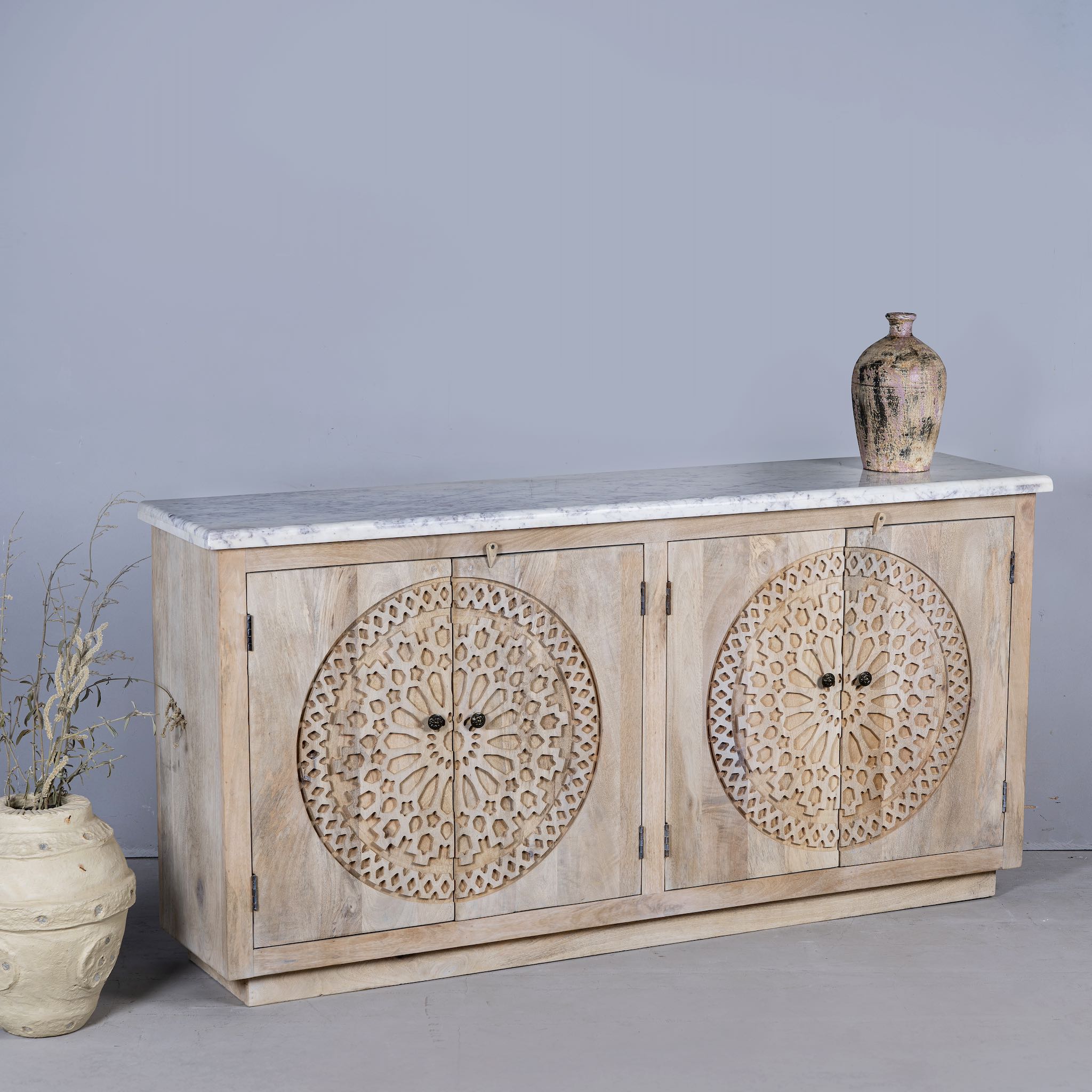 Side view of a Acacia wood sideboard with circular carvings, 4 doors and iron handles with a white marble top.