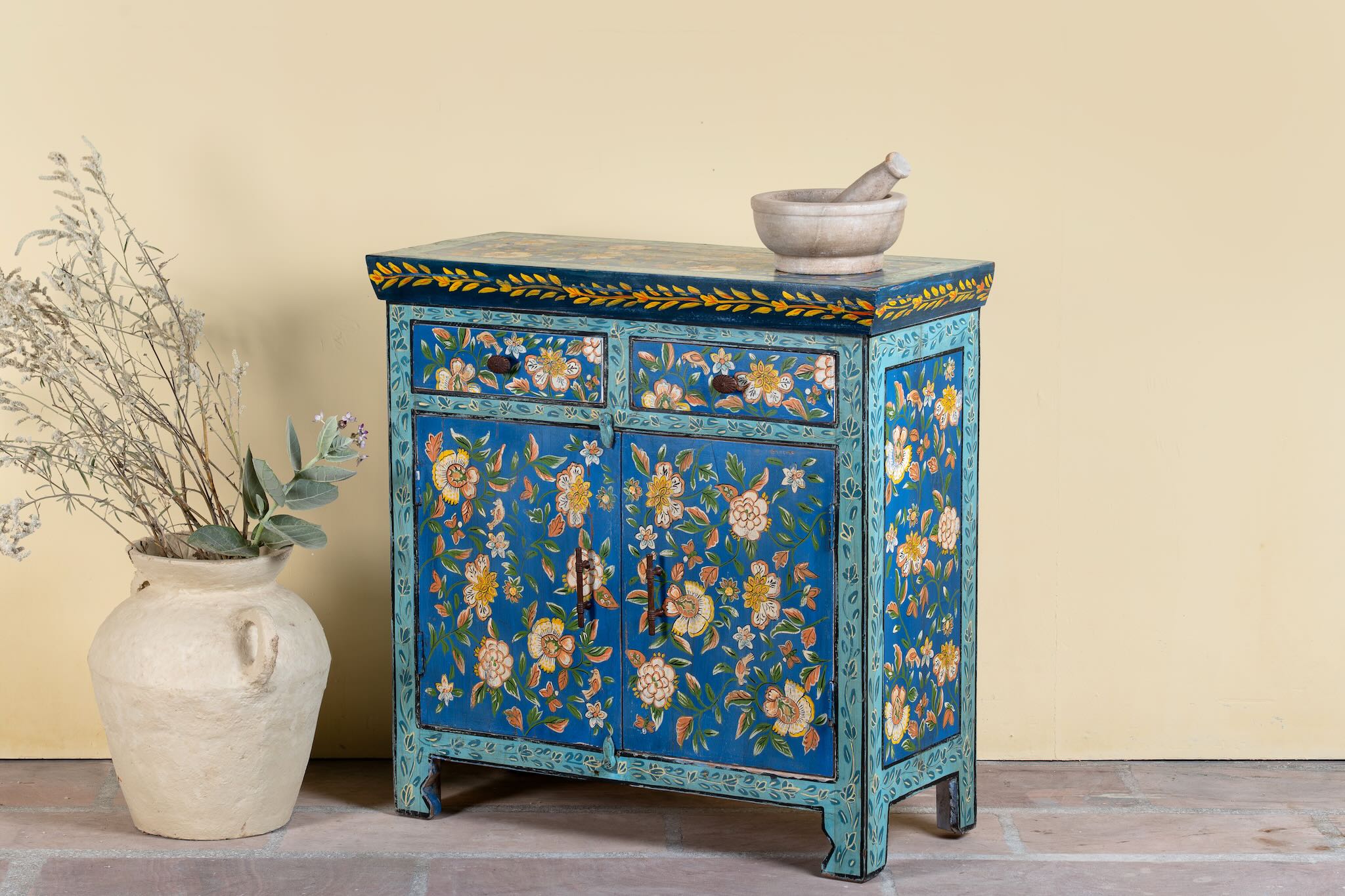 Side anle image of a hand-painted cupboard made of reclaimed wood with vibrant floral design – Tvesa model by Om Home & Garden