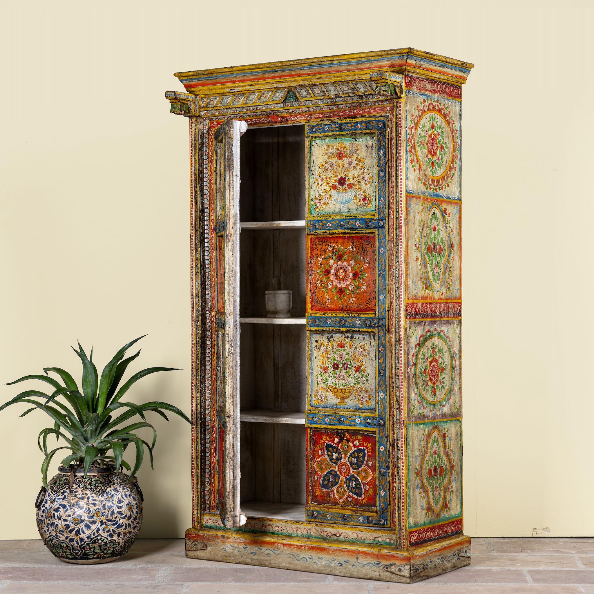 Side angle image of a hand-painted teak wood cabinet with floral motifs; teak wood furniture for bohemian interiors, 105 × 55 × 177 cm.