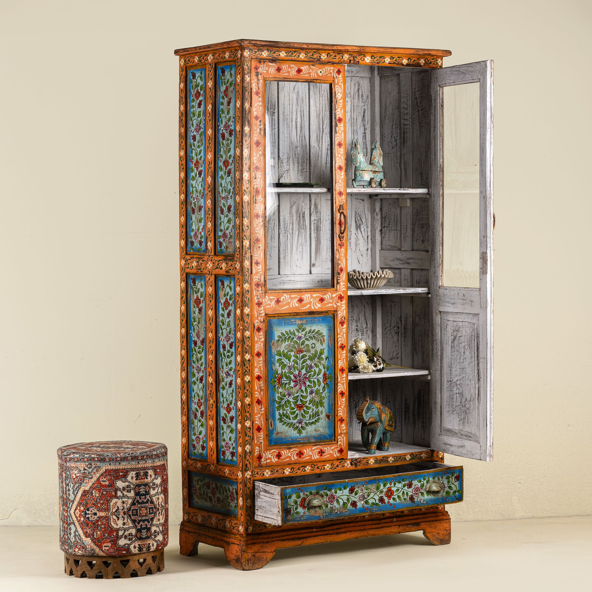 Side angle image with open door of a hand-painted teak wood showcase with floral motifs and glass doors – sustainable furniture crafted from recycled wood with traditional Indian artistry.