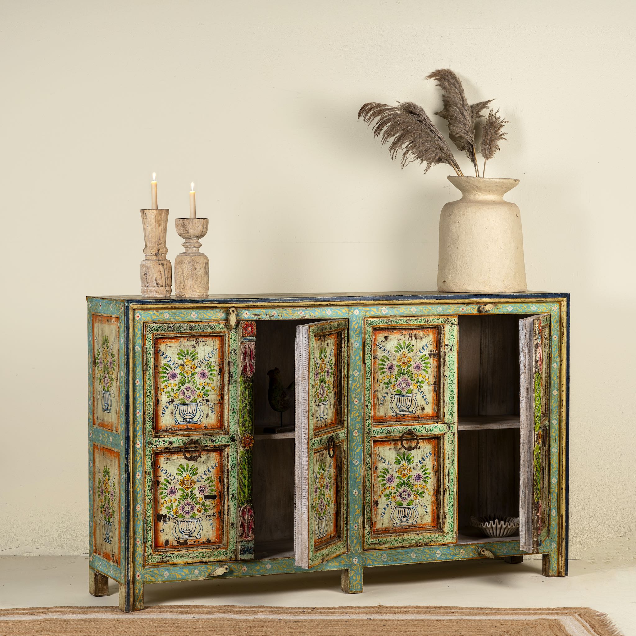 Open door image of a hand-painted sideboard made from reclaimed wood, showcasing vibrant floral motifs in green, pink, yellow, and blue on a distressed turquoise base, with six paneled doors and rustic iron ring handles.