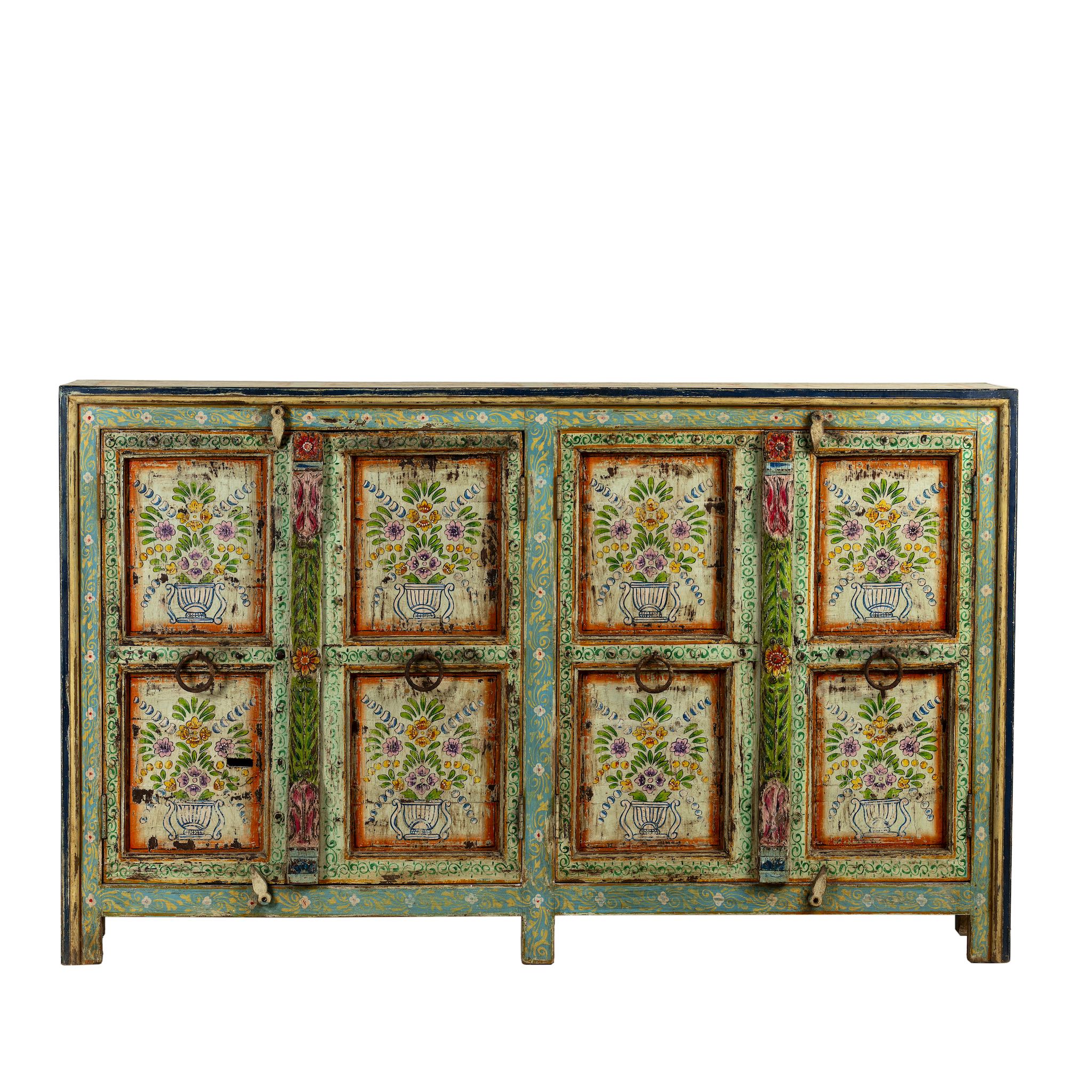 White background image of a hand-painted sideboard made from reclaimed wood, showcasing vibrant floral motifs in green, pink, yellow, and blue on a distressed turquoise base, with six panelled doors and rustic iron ring handles.