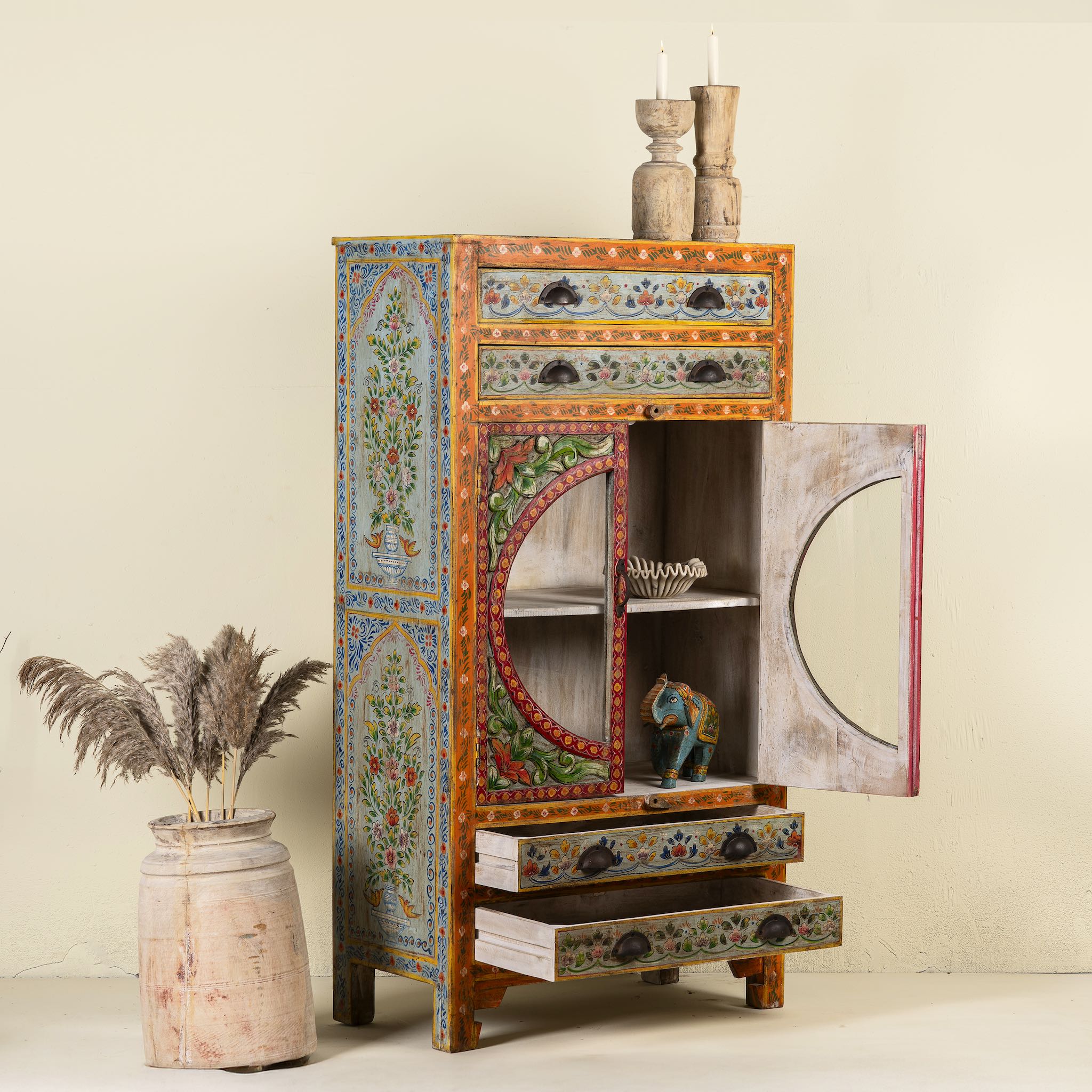 Open door view of a hand-painted showcase cabinet made from mango wood, featuring a circular glass-front display, floral motifs in rich orange, green, and red tones, and five drawers for added storage.