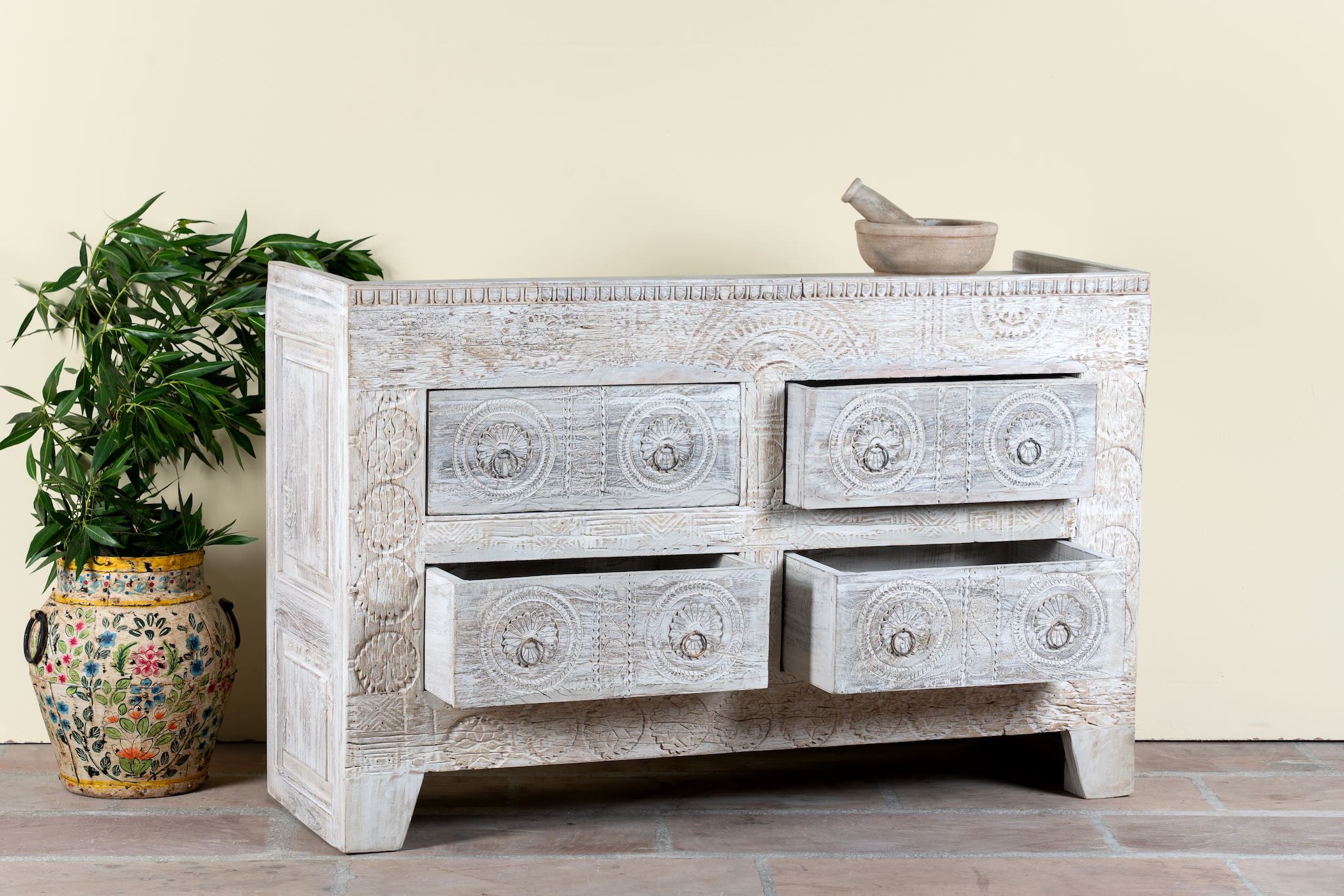 Side angle image with open drawers of a handcrafted chest of drawers Zuber made from reclaimed wood, featuring four carved drawers with circular motifs and a whitewashed finish. A rustic, sustainable furniture piece with soft texture and elegant detailing.