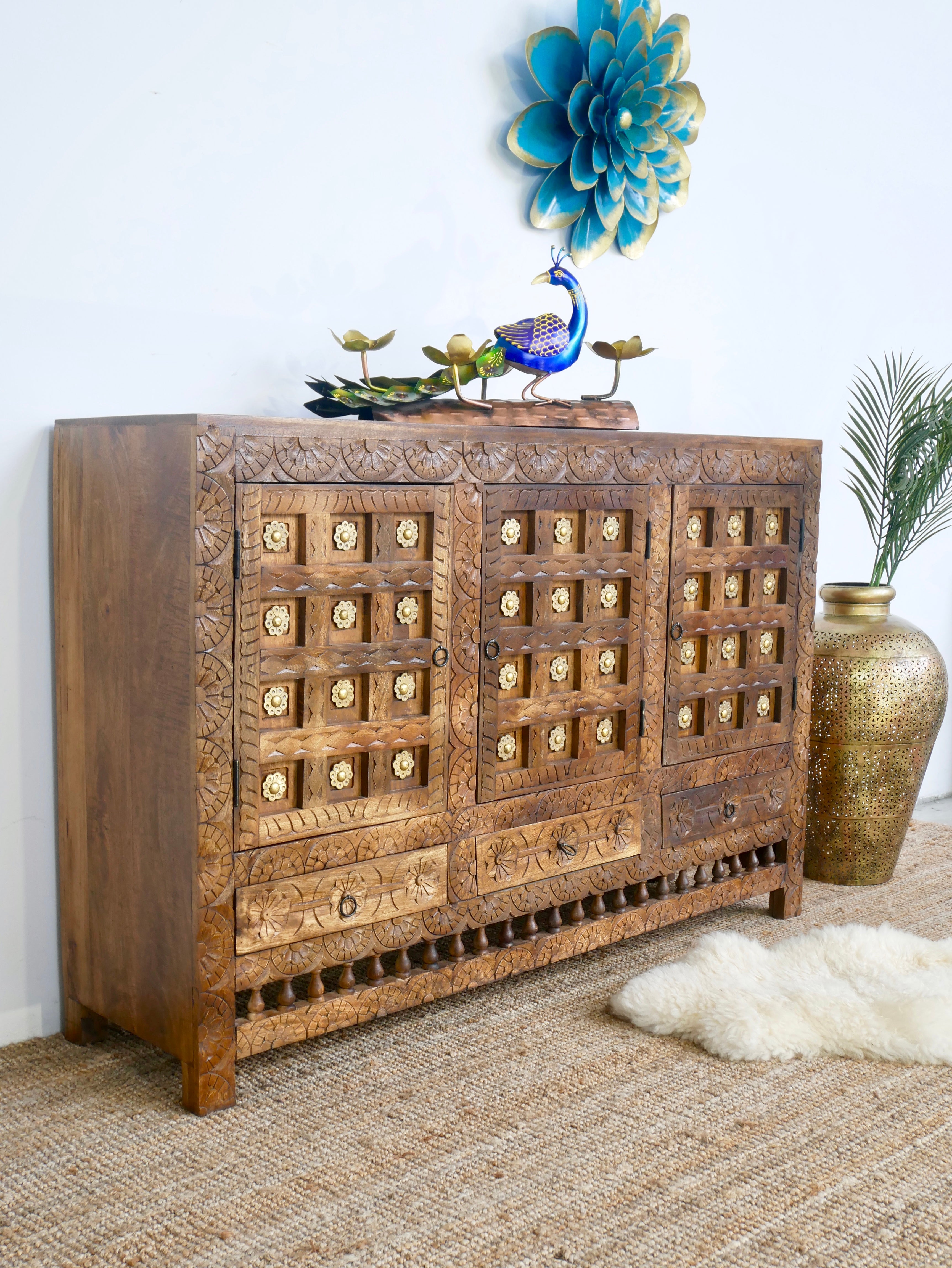 Side angle image of a handcrafted traditional sideboard made from mango wood with Indian carvings and brass inlay; Indian furniture, 150 × 100 × 40 cm.