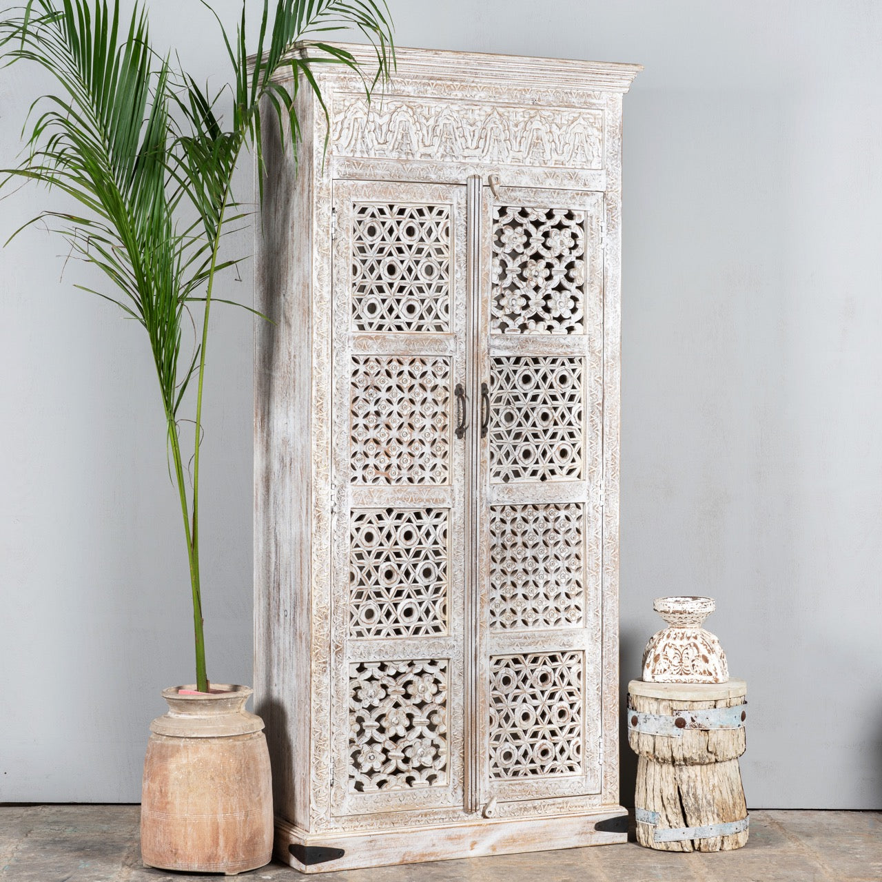 Side angle image of a Hand-carved mango wood wardrobe with whitewashed finish, bedroom furniture wooden wardrobe with floral and geometric lattice doors, 90 × 190 × 40 cm.