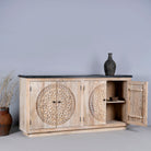 Open door view of an acacia wood sideboard with 4 doors and iron fitted door knobs with floral round carvings and a black marble top.