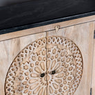 Close up view of an acacia wood sideboard with 4 doors and iron fitted door knobs with floral round carvings and a black marble top.