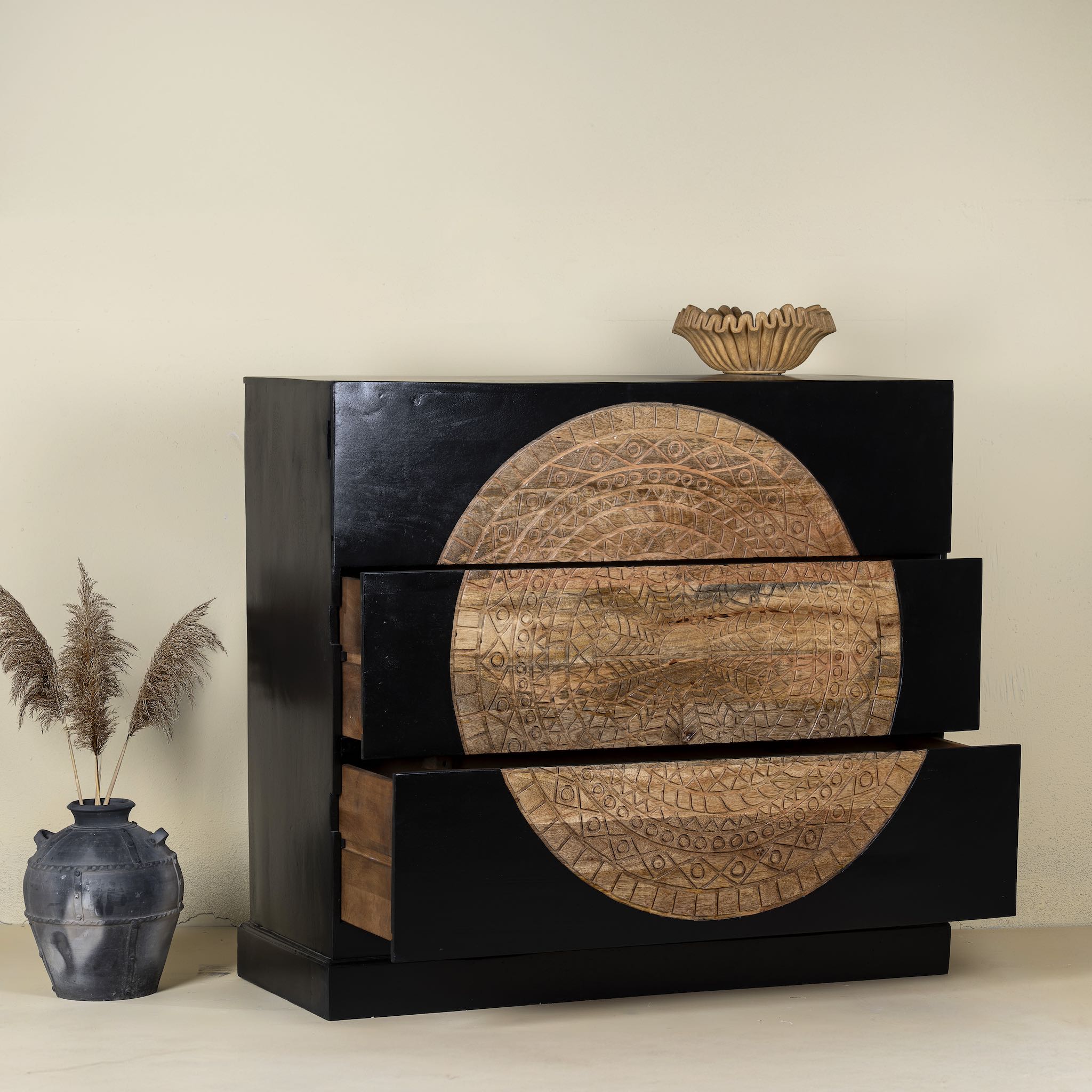 Side angle image with open drawer of a mandala carved wood chest with black frame and natural carved mango wood drawers, mango wood drawer chest for modern bohemian interiors, 120 × 47 × 110 cm.