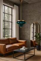 Lifestyle image of a a large green glass pendant light with a brass plated frame and a metal rod attachment.