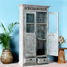 Side angle image with open door of a reclaimed teak wood cabinet in shabby chic white with glass doors and ceramic inlays – dining room furniture with vintage elegance.