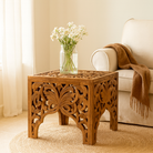 Lifestyle imagination of a square hand carved coffee table made from solid mango wood with intricate detailing; compact and rustic, 50 × 50 × 40 cm.