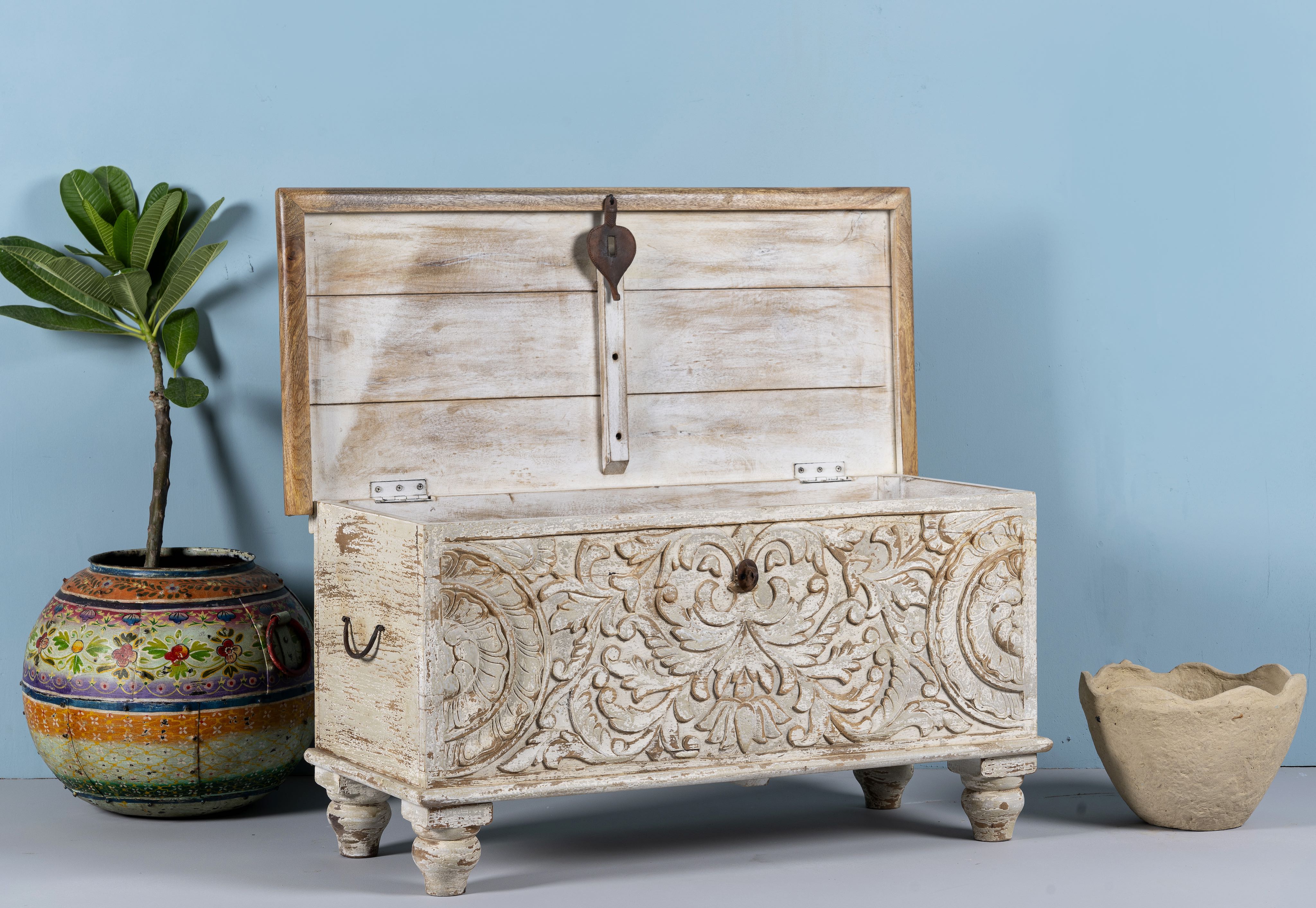 Side angle image with open lid of a hand-carved mango wood chest box with floral whitewashed detailing and iron handles – vintage home accessory and unique furniture with rustic charm.