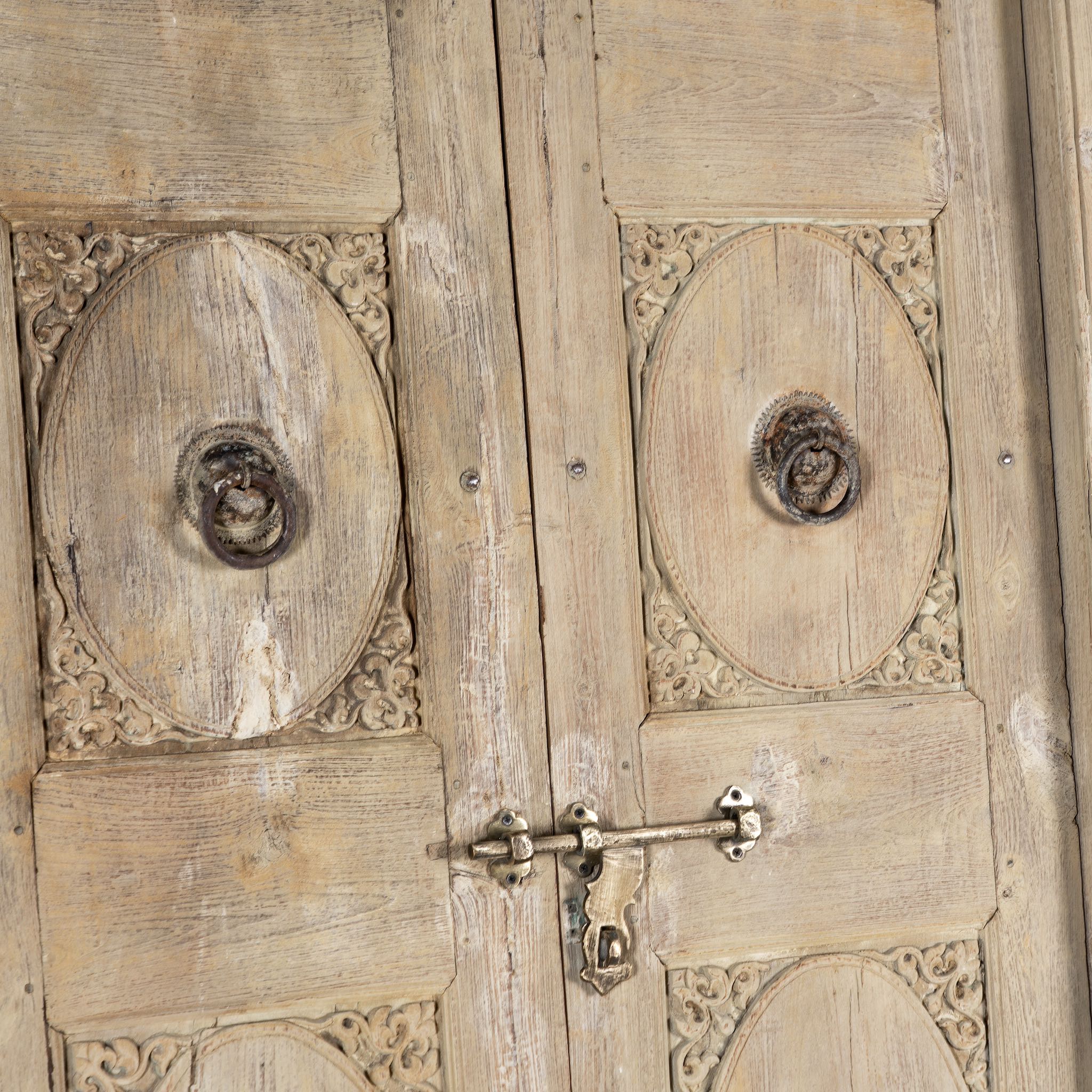 Close up image of a heavy reclaimed Indian teak door with unique hand carvings, sandblasted finish, and original brass hardware, extended to fit European height within a restored frame.