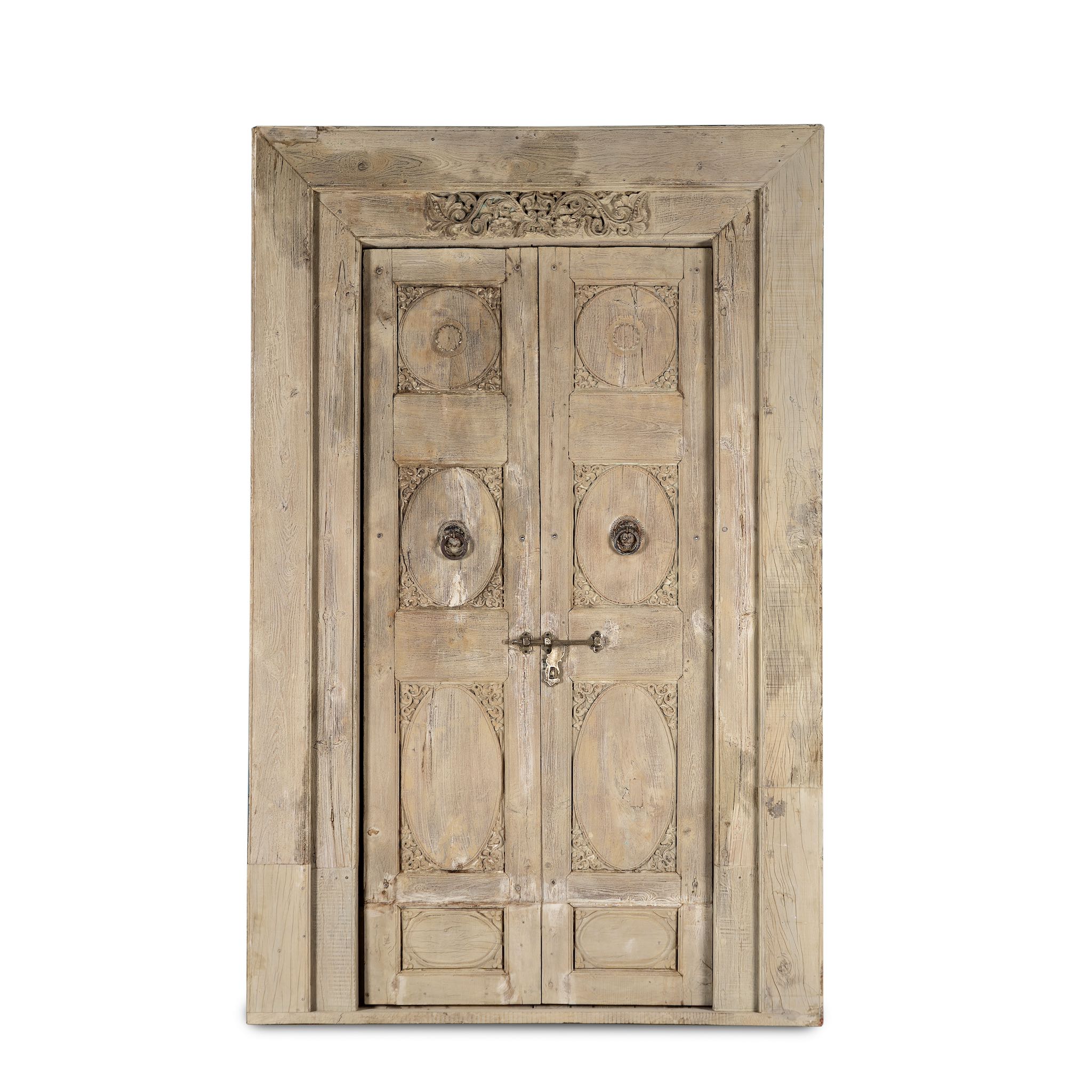 White background image of a heavy reclaimed Indian teak door with unique hand carvings, sandblasted finish, and original brass hardware, extended to fit European height within a restored frame.